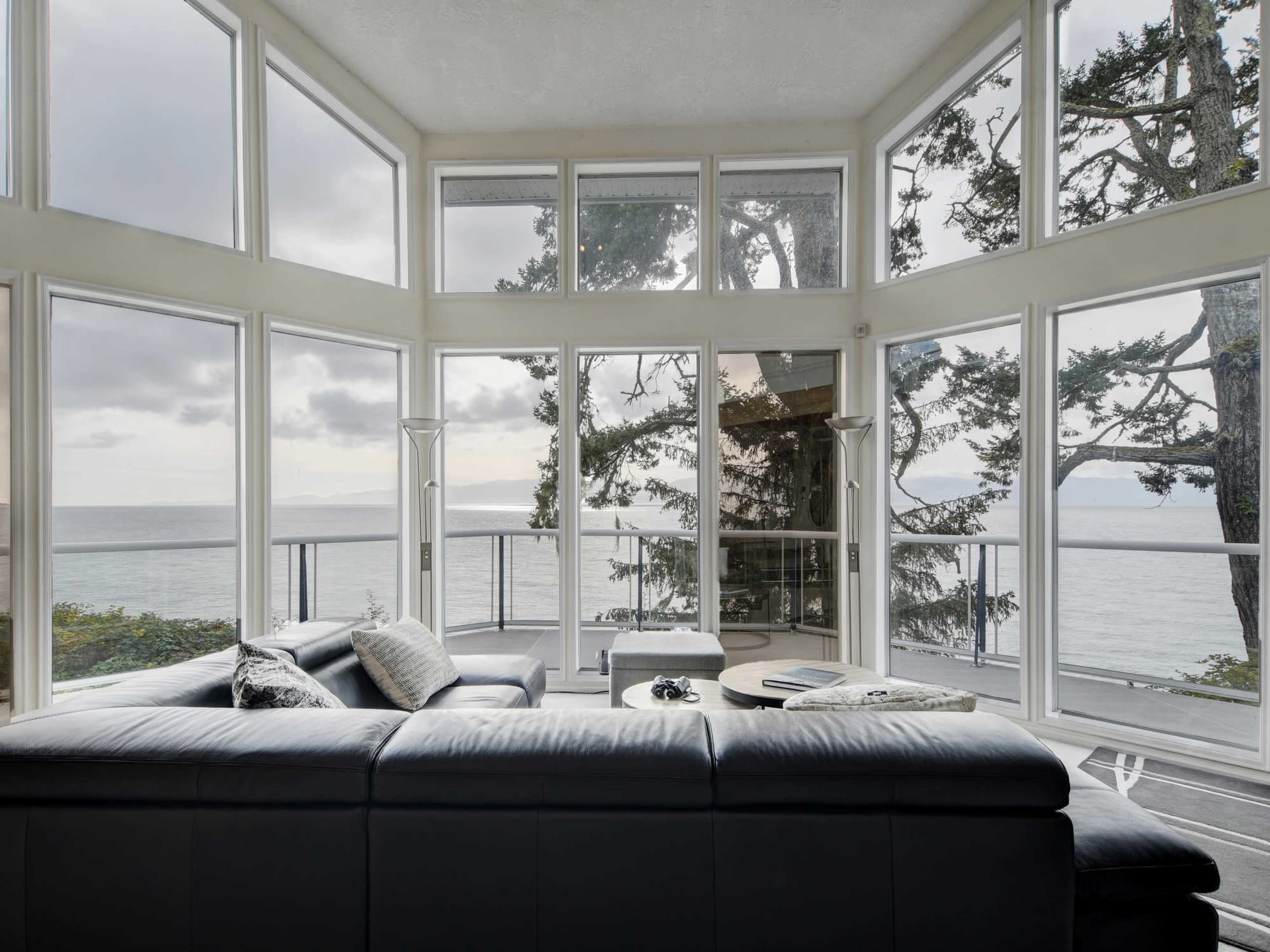 A modern living room features large windows overlooking a body of water and trees.