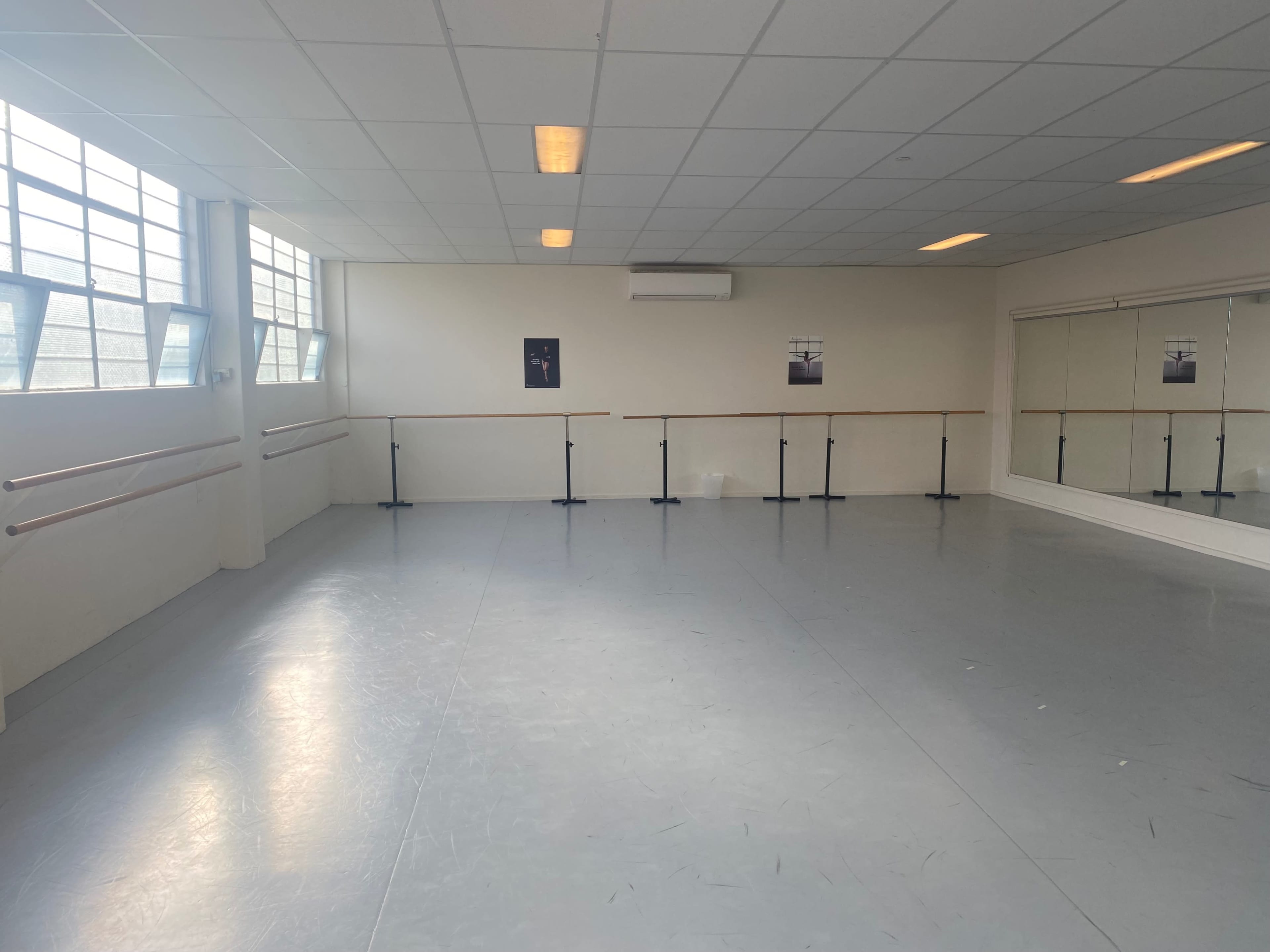 A spacious dance studio with a mirrored wall, ballet barres, and large windows allowing natural light to enter.