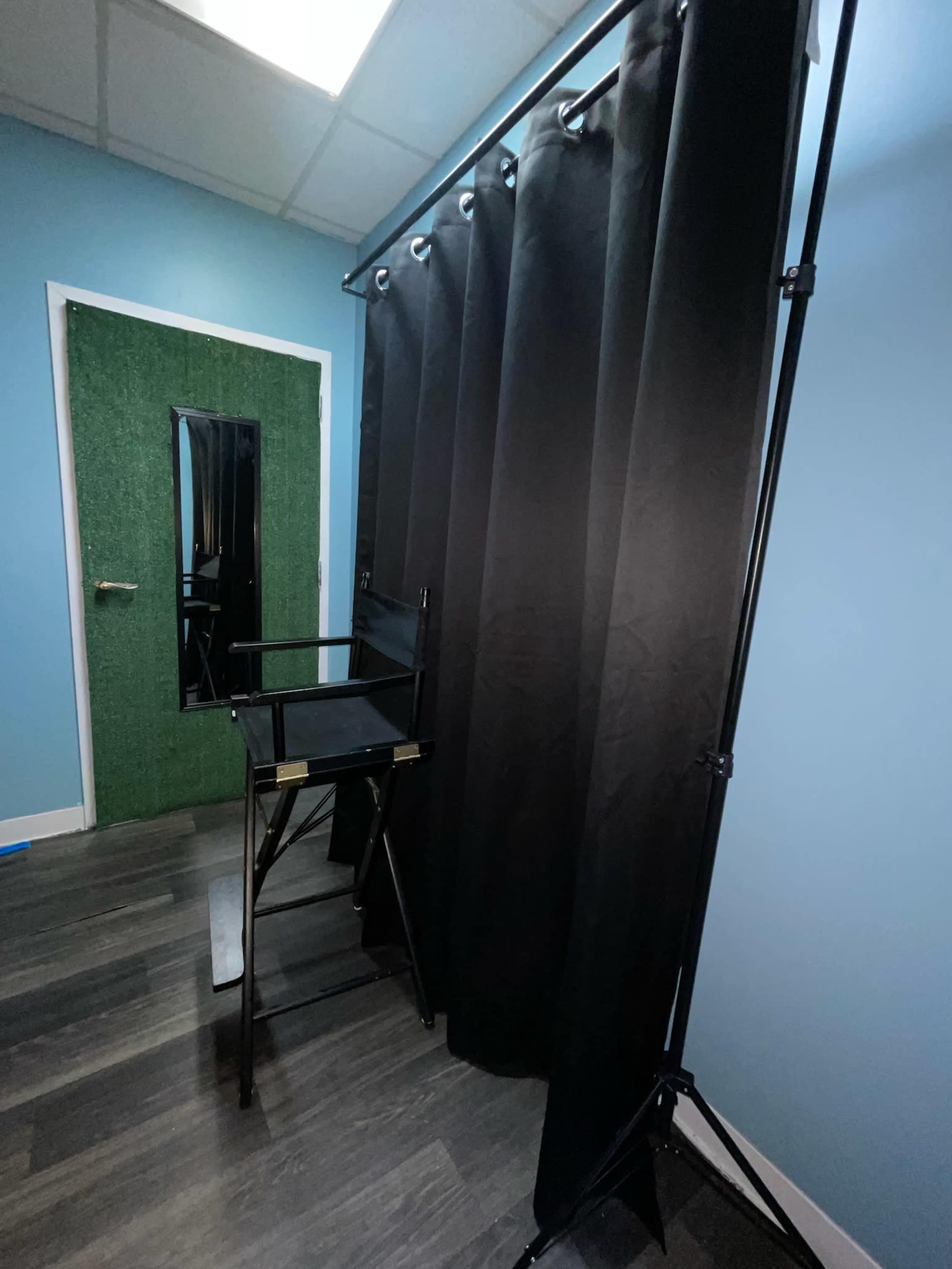 The image shows a black curtain setup with a director's chair in a room featuring a green door and blue walls.