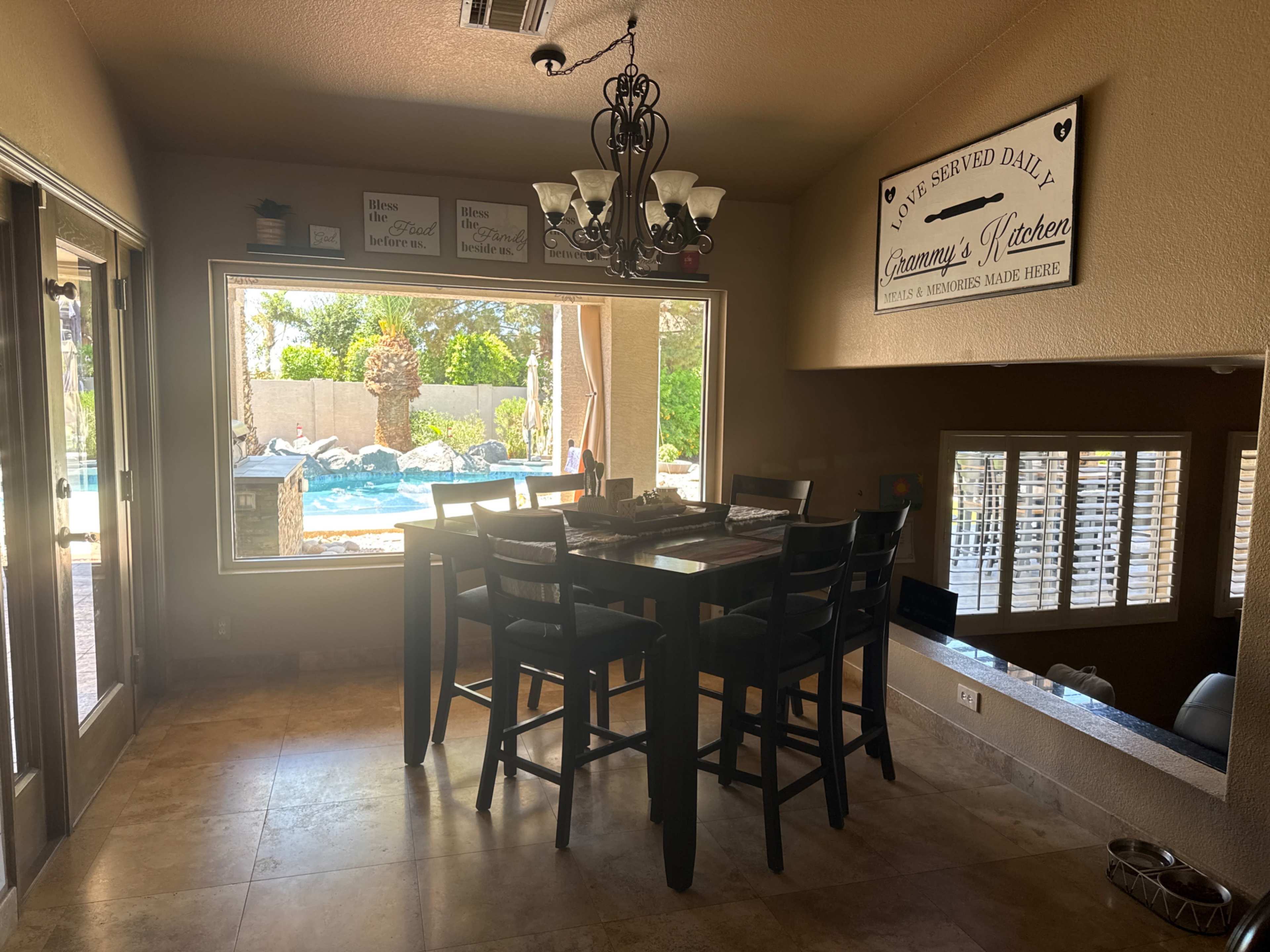 A dining area features a tall black table with chairs, surrounded by large windows overlooking a backyard pool and patio space.