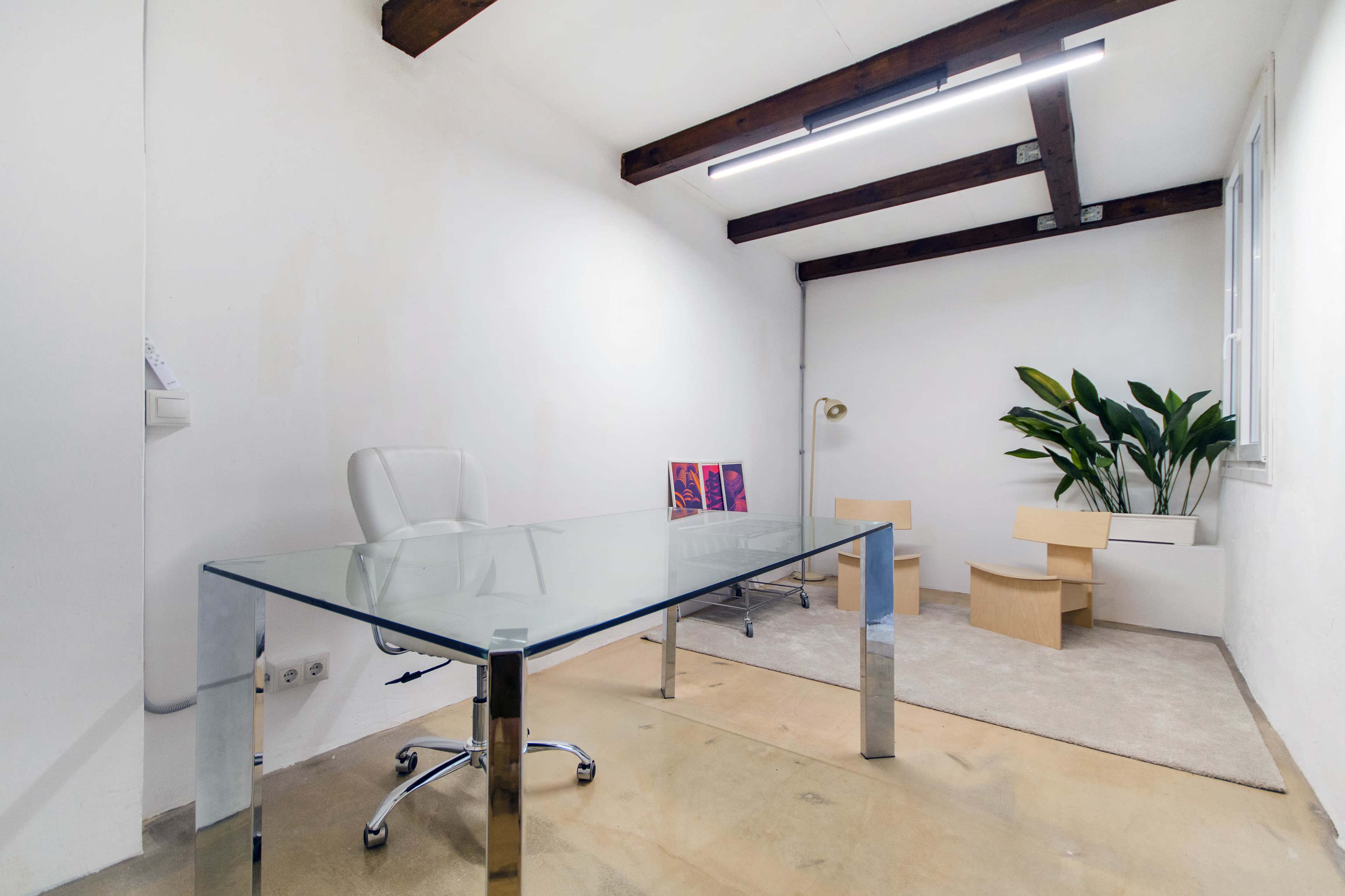 The image shows a minimalistic office space featuring a glass desk, a white chair, and modern wooden elements, along with a potted plant and a small seating area.
