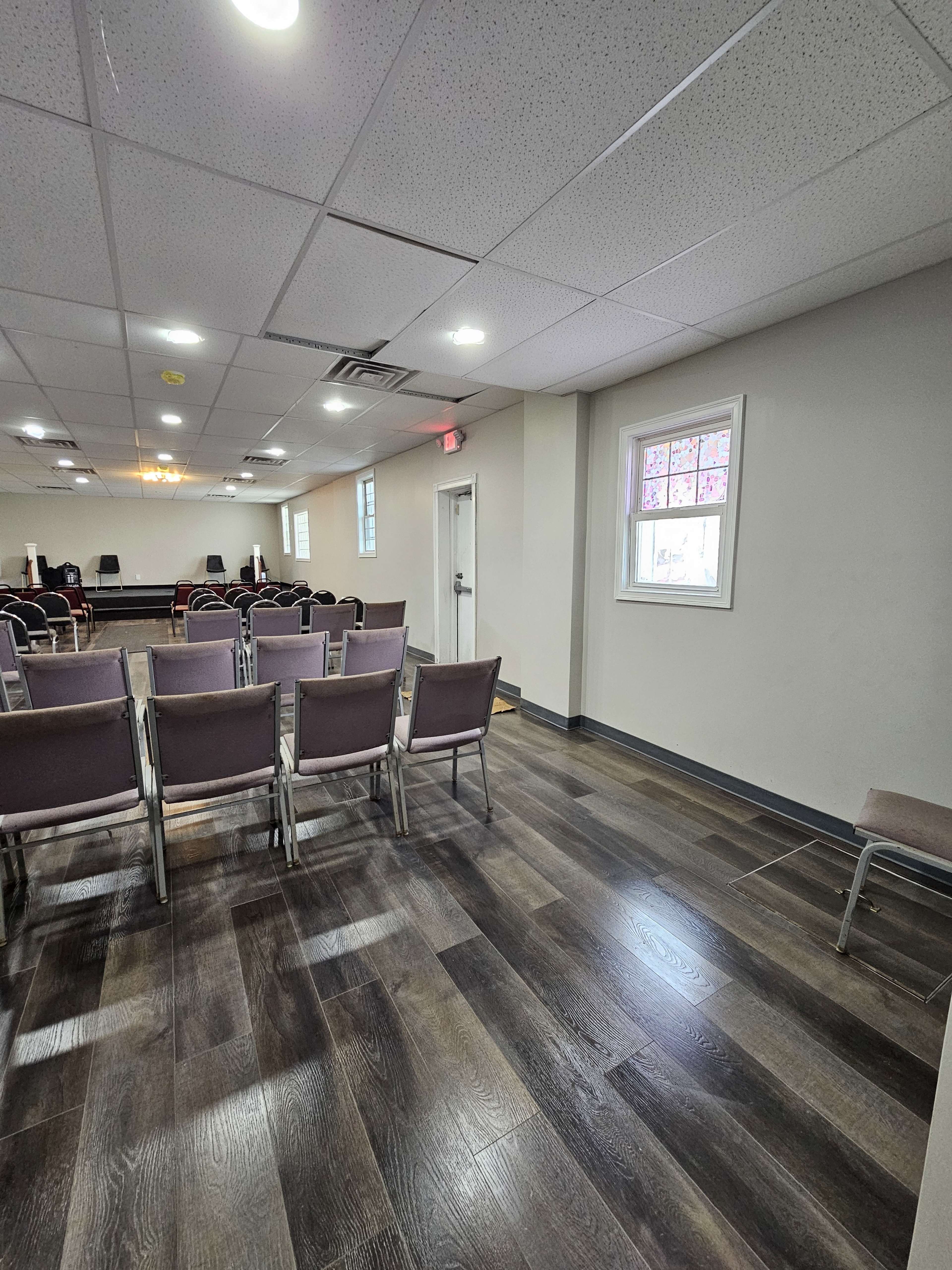The image shows a meeting room with rows of empty chairs arranged facing a stage area, and a window on the right side.