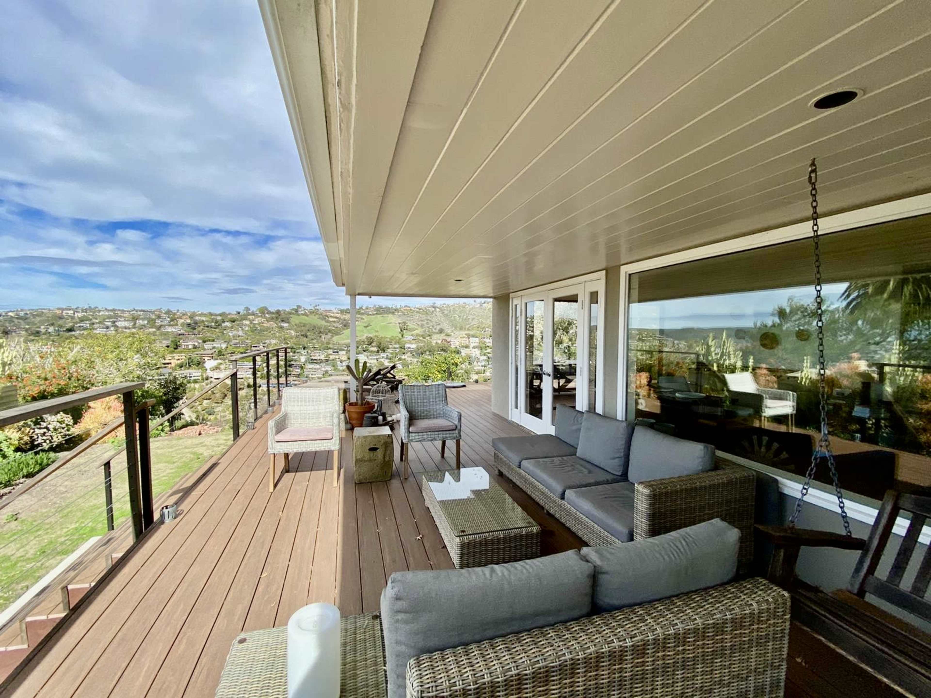 A covered patio features wicker furniture and offers a view of a landscaped hillside under a cloudy sky.