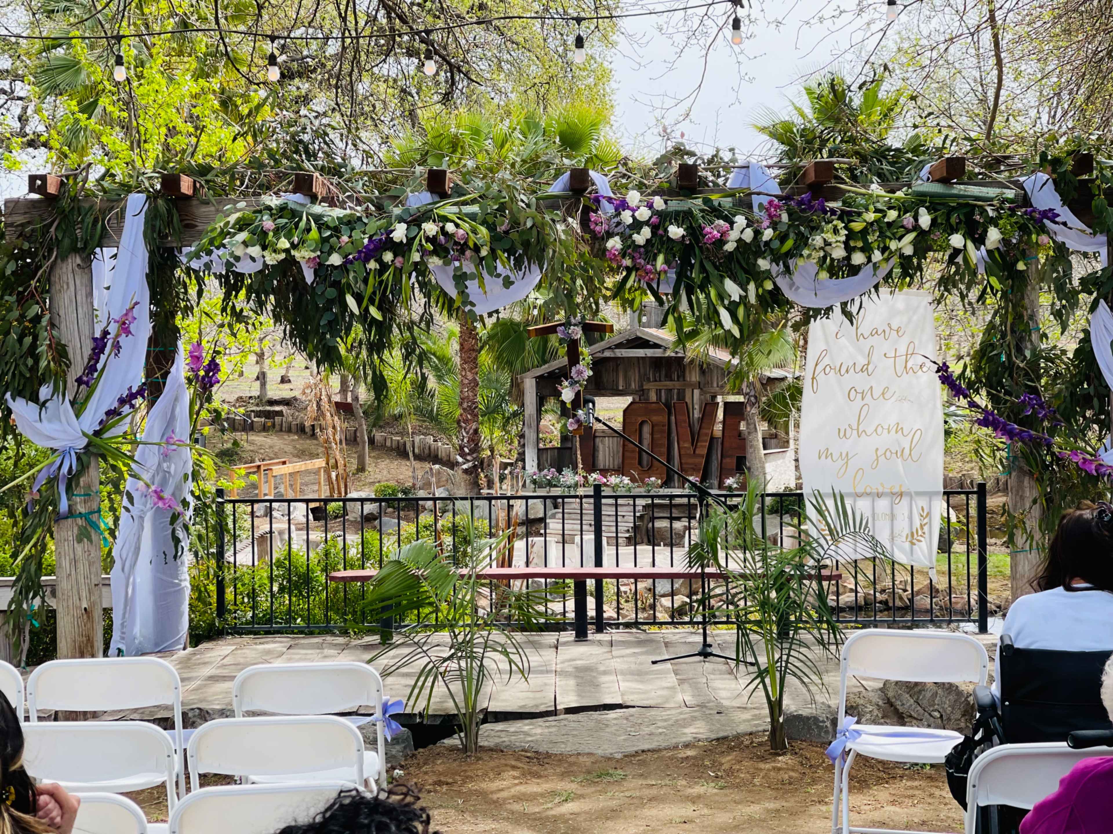 A wedding ceremony setup with a floral arch and white chairs arranged in front of a rustic backdrop.