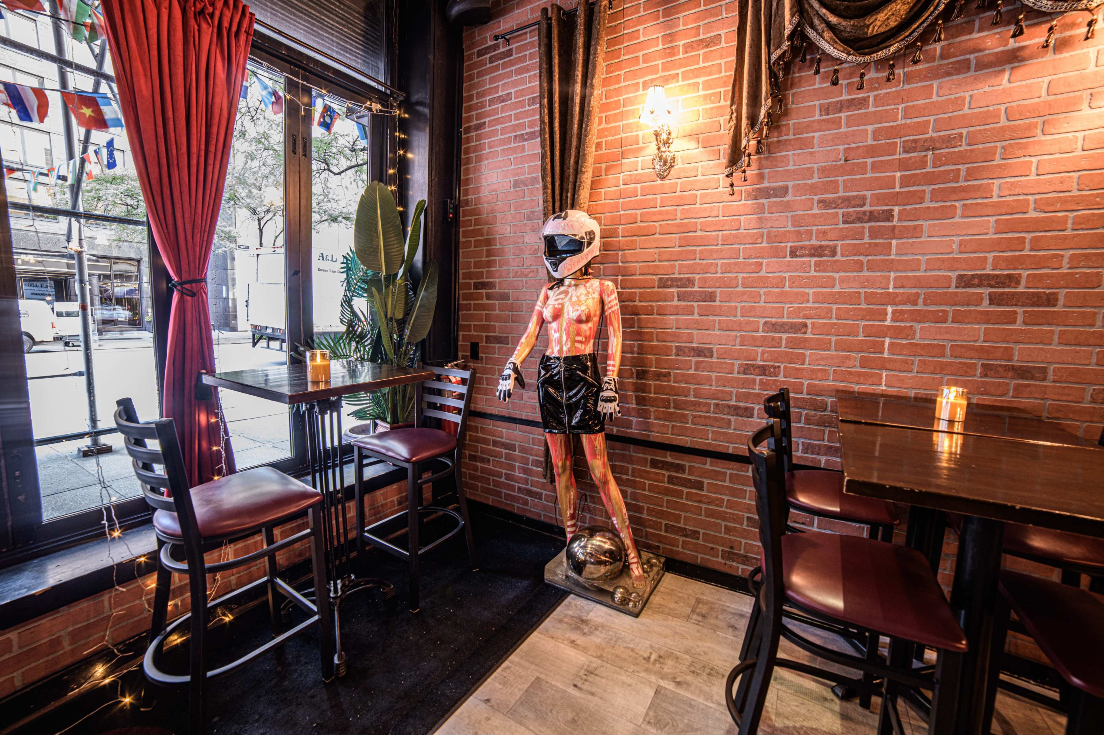 The image shows a bar interior with brick walls, a plant, and a metallic figure wearing a helmet and boxing shorts standing near a table.