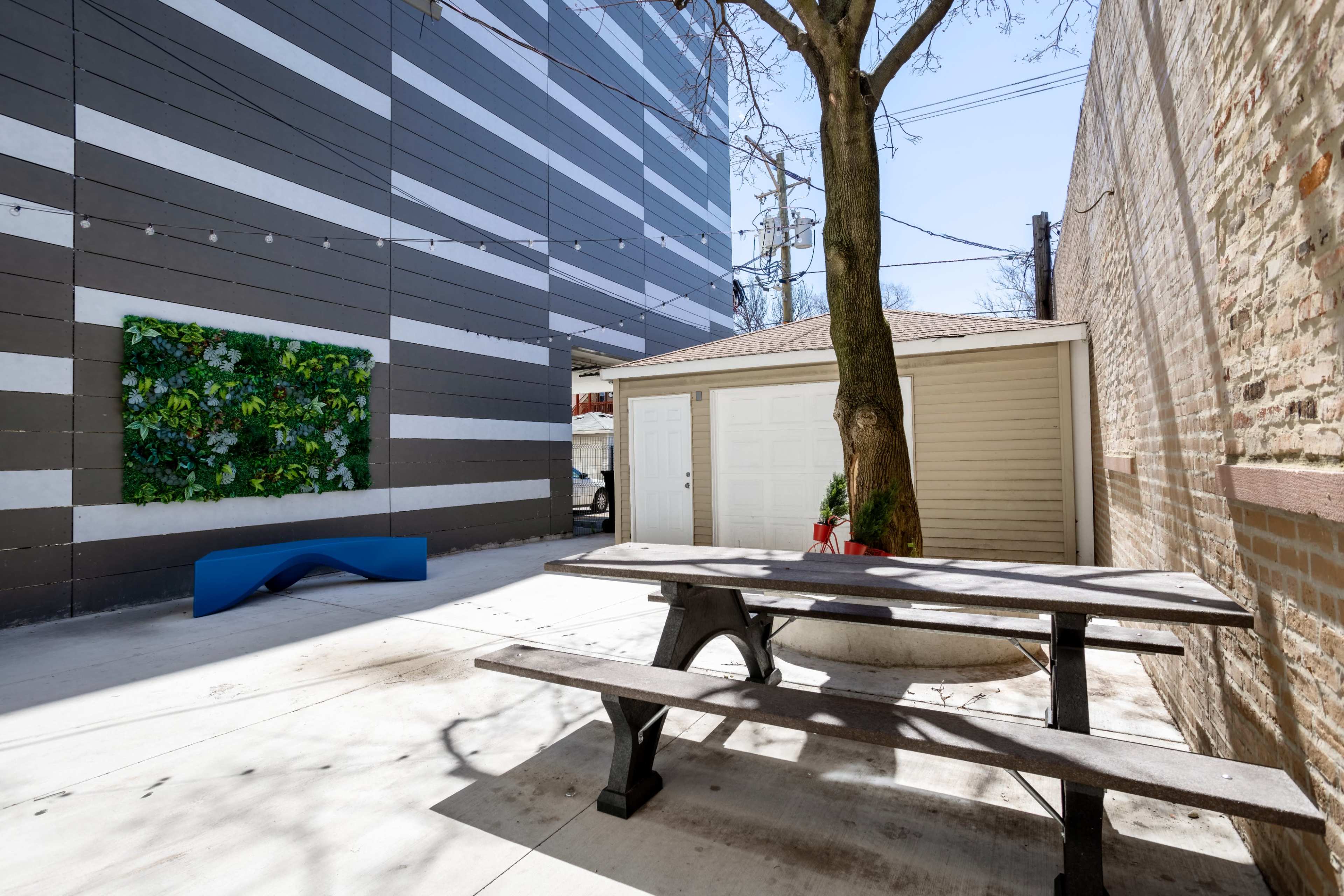 A small outdoor space features a picnic table, a storage shed, a wall with vertical greenery, and a tree.