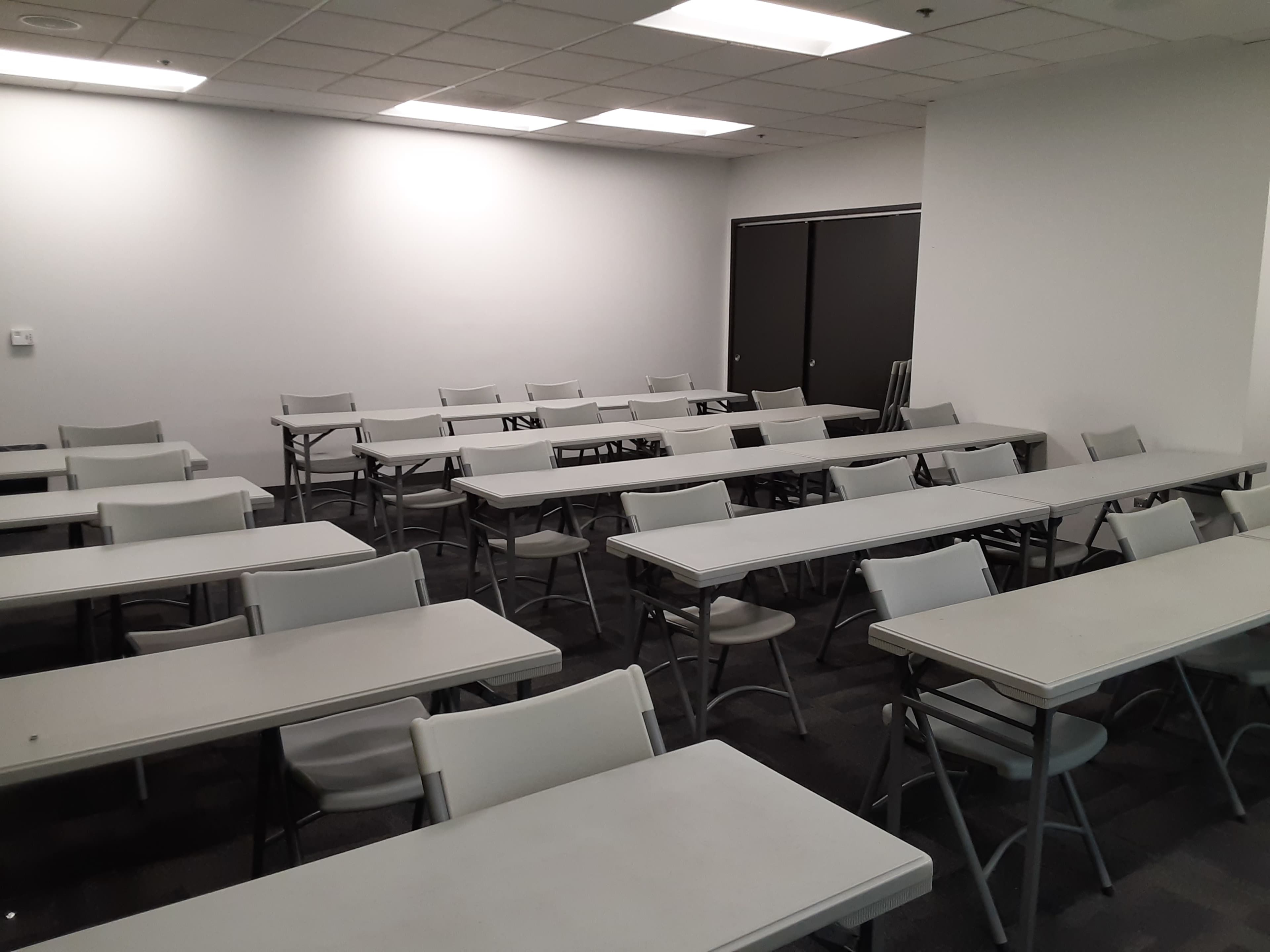 An empty classroom arranged with multiple rows of tables and chairs.