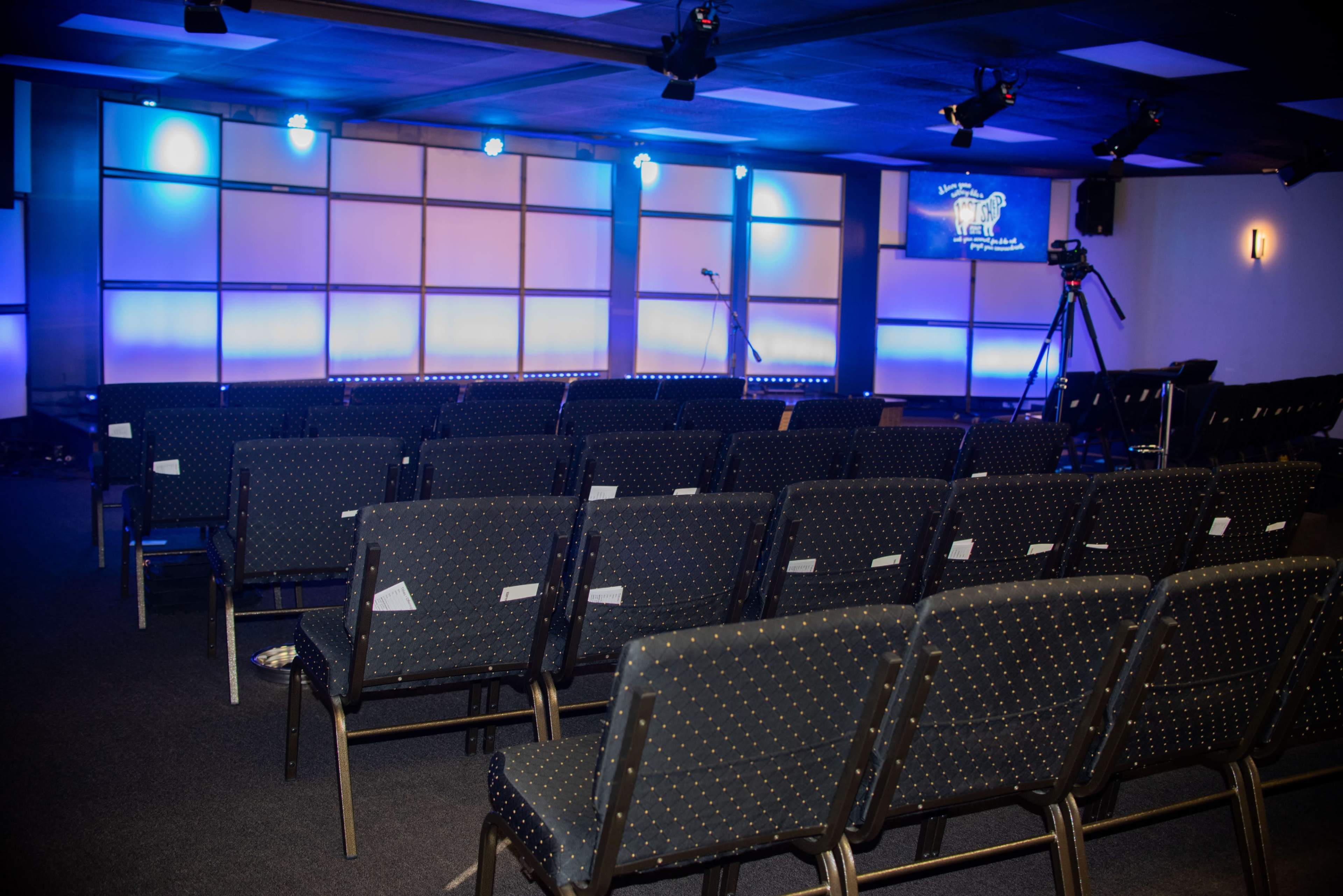 A neatly arranged seating area with rows of chairs facing a stage illuminated by blue lighting.