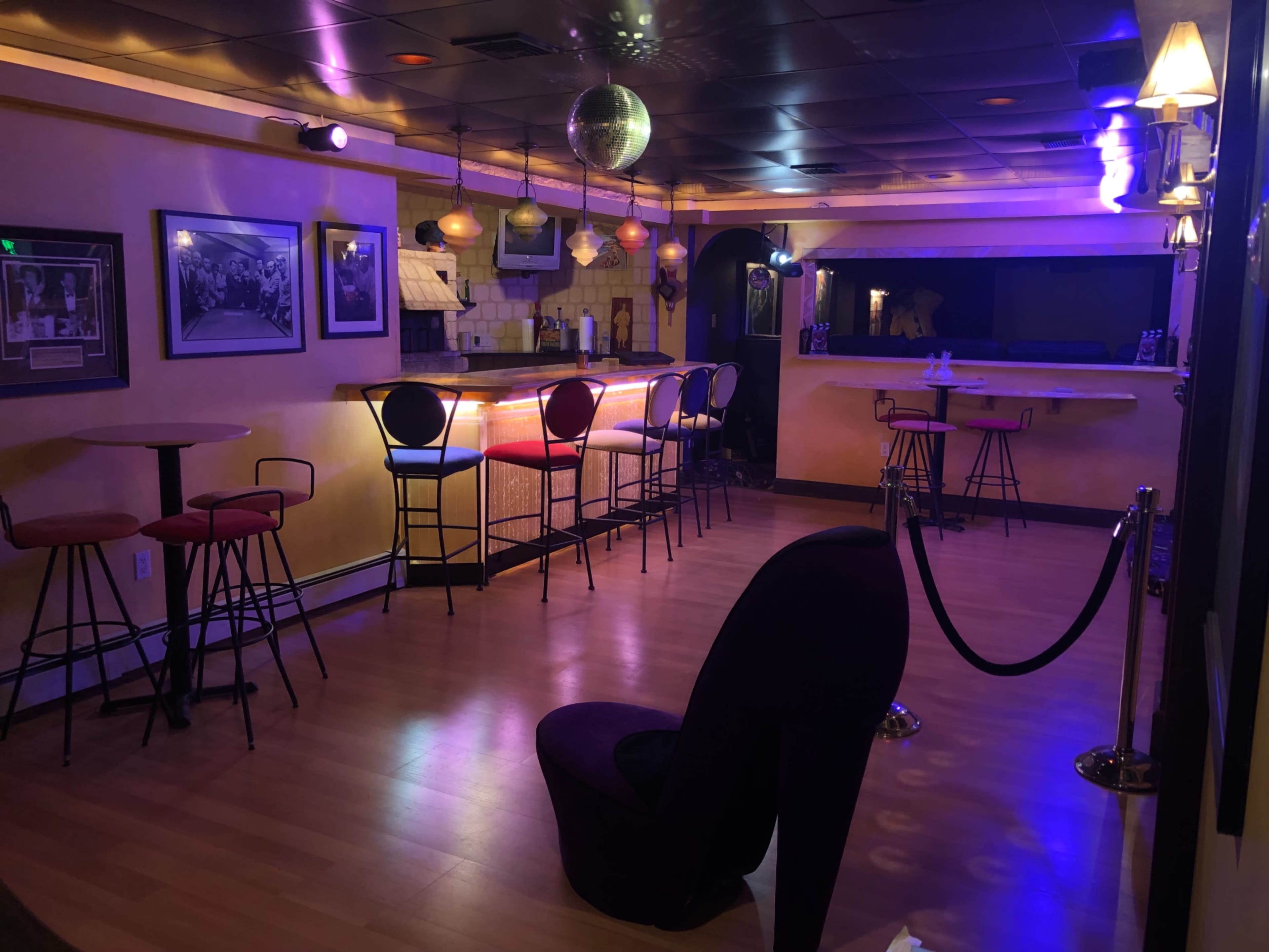 A dimly lit bar area with a disco ball, several tables and stools, and a brightly illuminated bar counter.