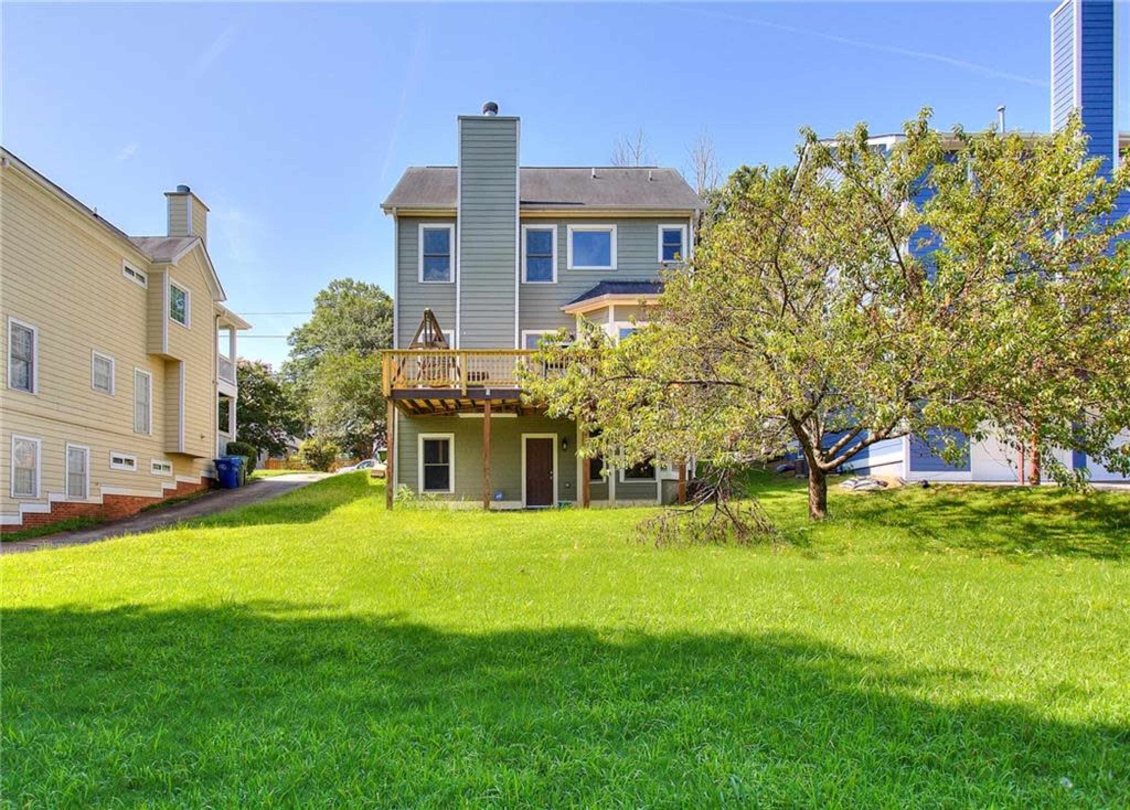 A two-story house with a wooden deck is situated in a grassy yard, surrounded by neighboring homes.