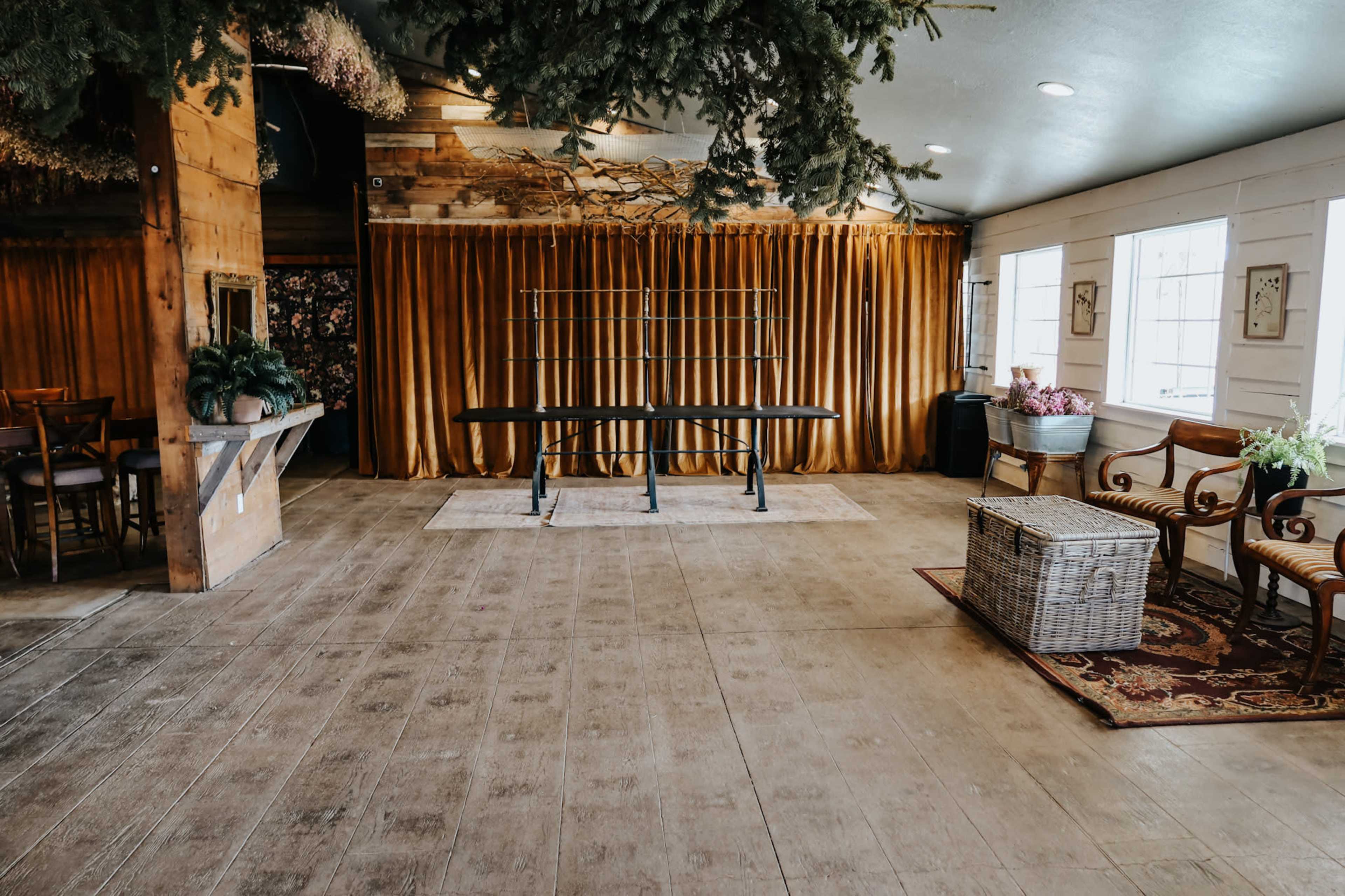 The image shows a spacious room with wooden floors, large curtains, and minimal furniture including a table and woven storage box.