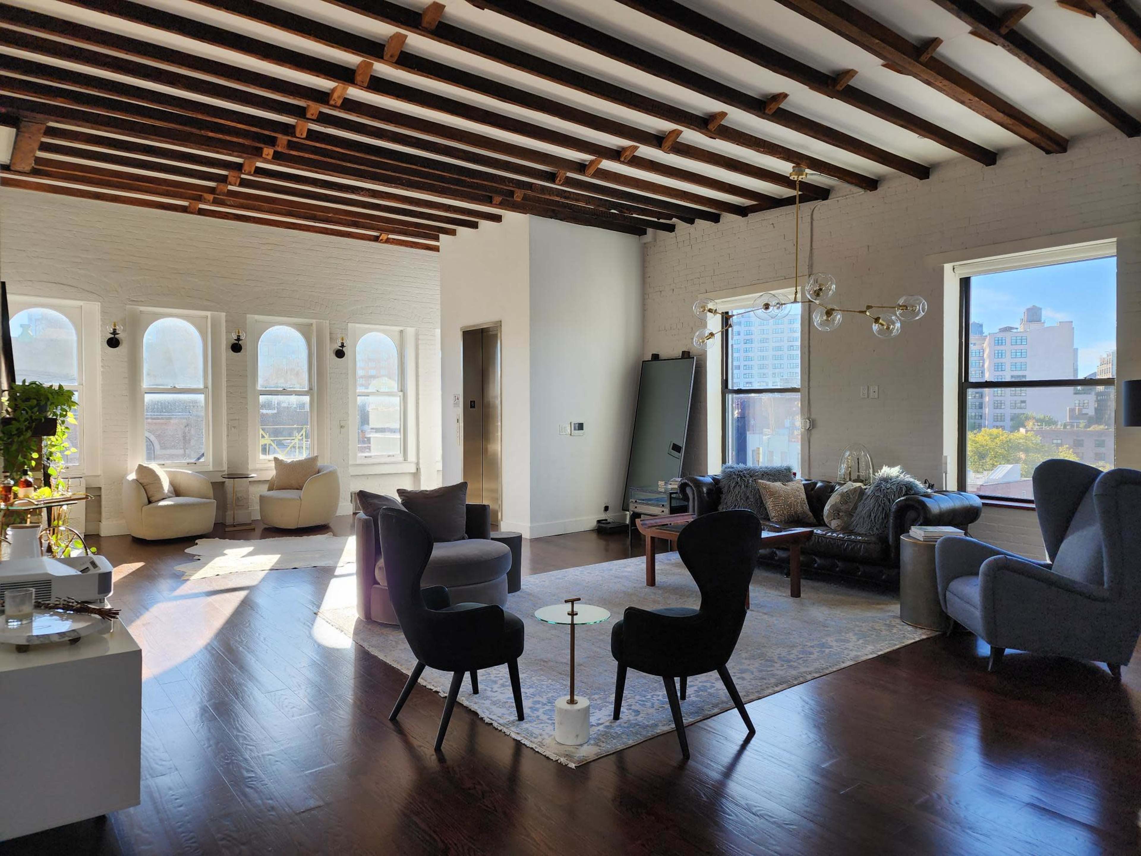 A spacious living room features modern furniture, large windows, and exposed wooden beams on the ceiling.