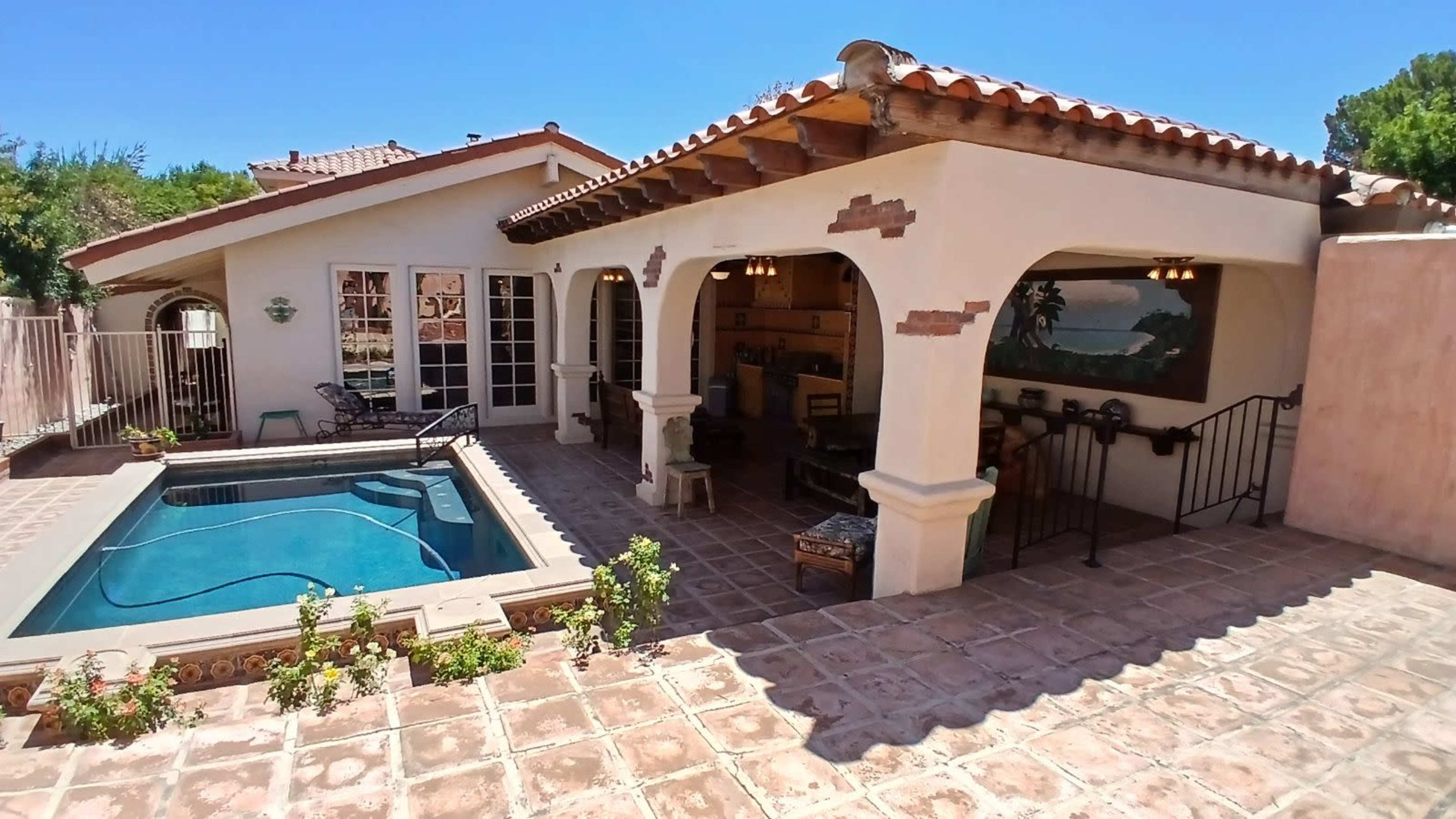 A spacious patio area featuring a swimming pool, surrounded by a tiled floor and an outdoor seating arrangement under a covered porch.