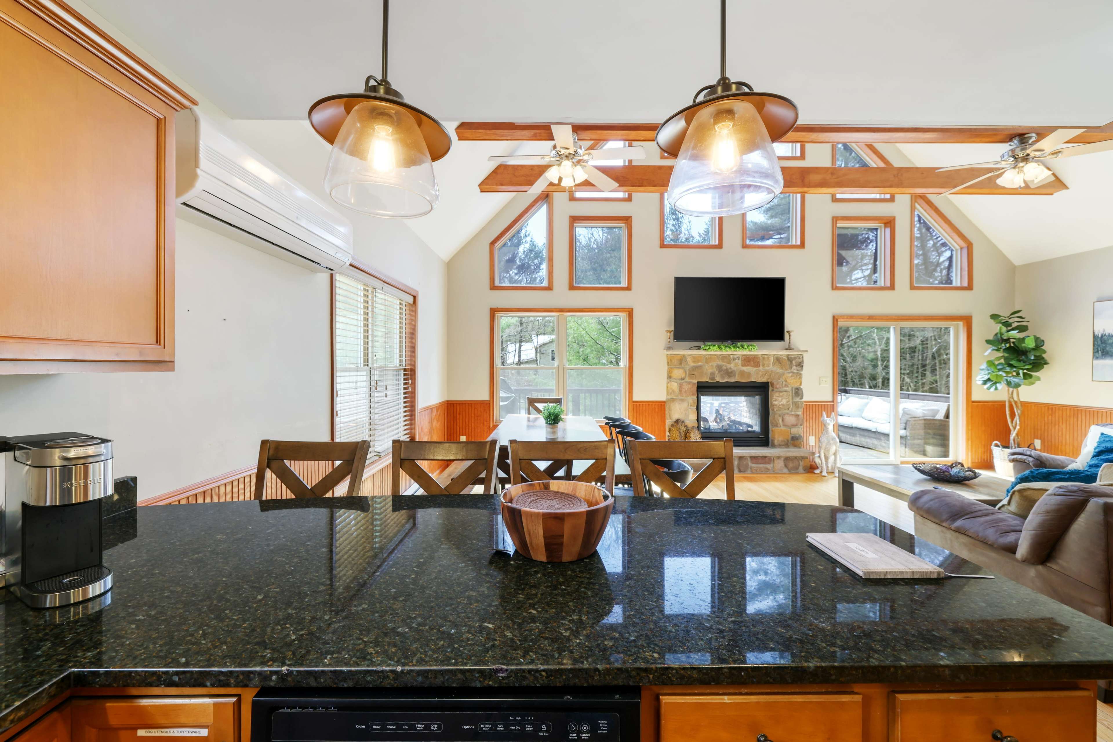 A kitchen with dark granite countertops overlooking a living area featuring a fireplace and large windows.
