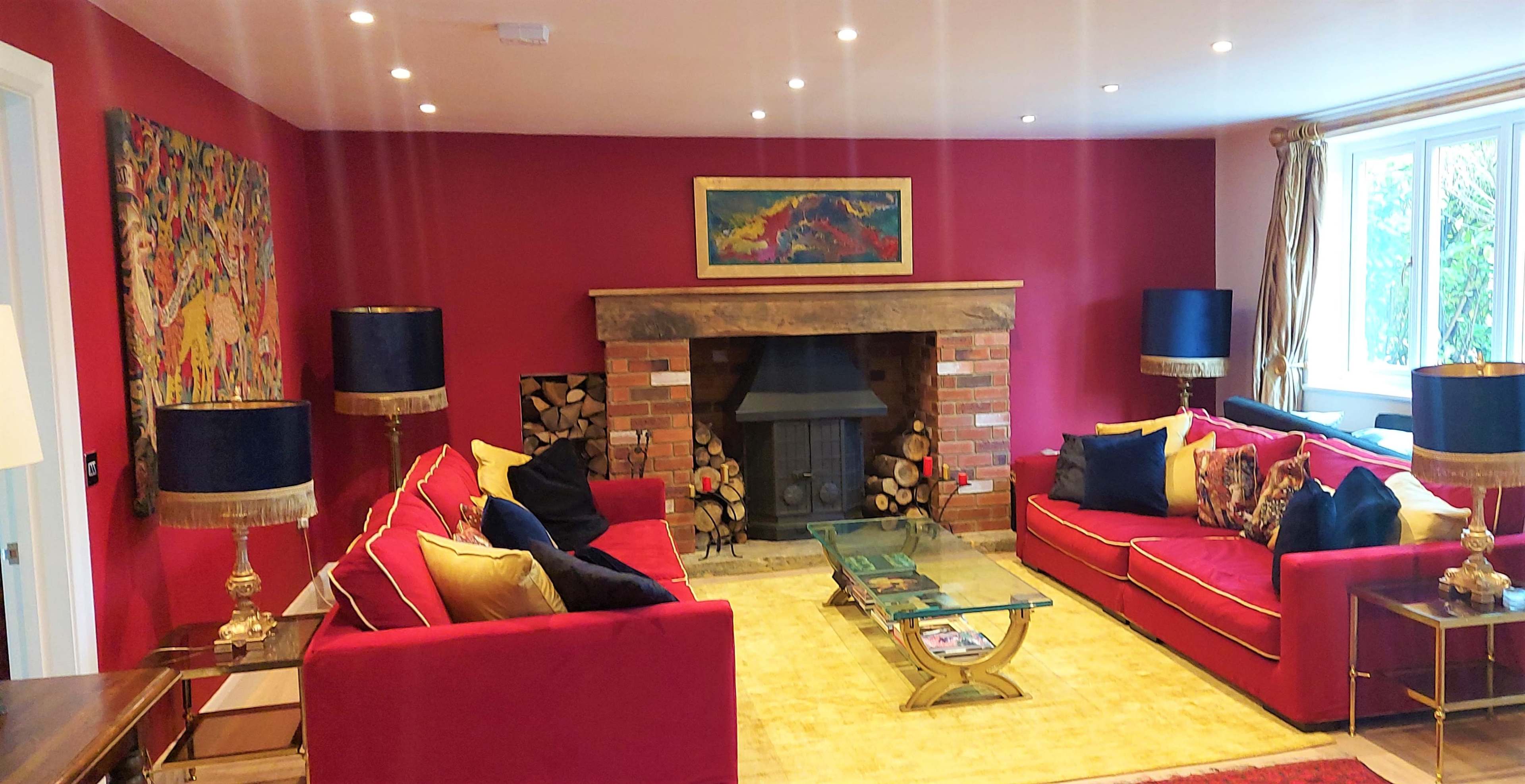 The living room features red walls, two red sofas with decorative cushions, a wooden fireplace with stacked logs, and a glass coffee table on a yellow rug.