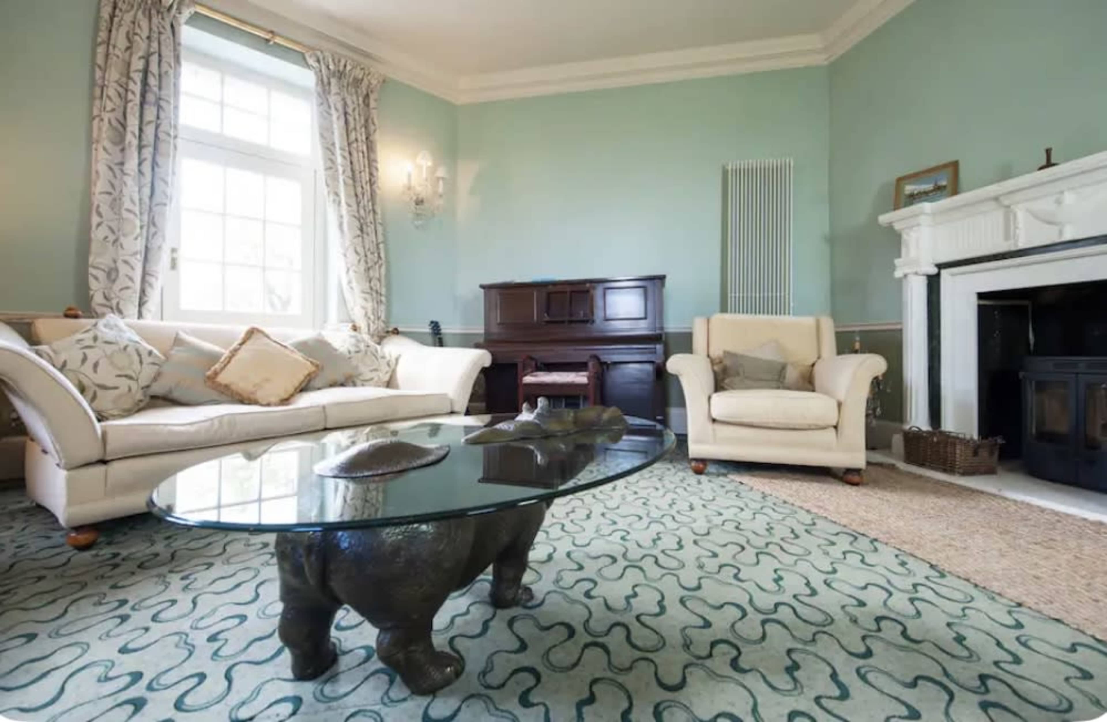 A cozy living room features a beige sofa and armchair, a glass table with a sculpted base, and a decorative rug on the floor.