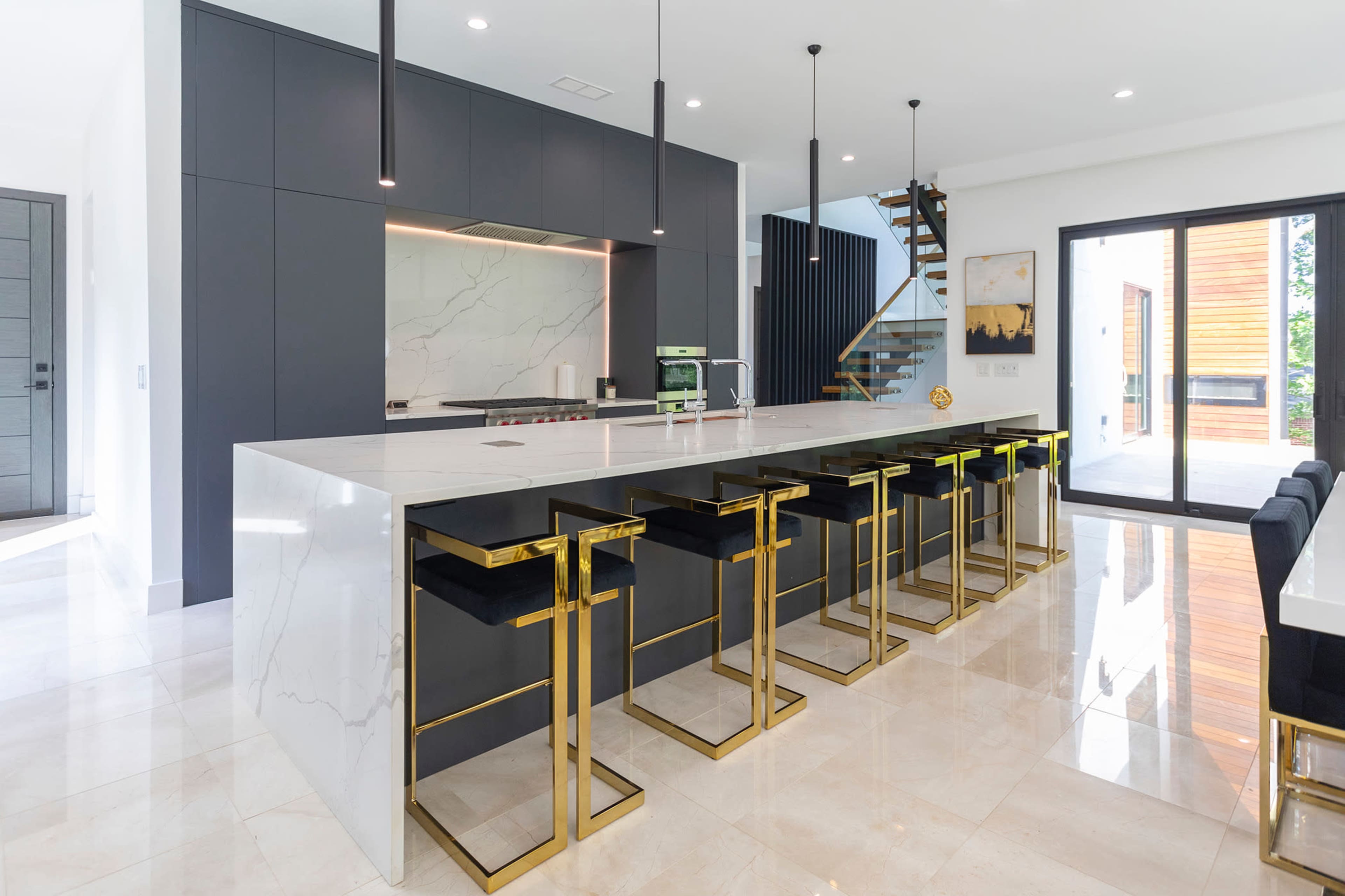 The image showcases a modern kitchen with a large marble island, black cabinetry, and gold-accented bar stools.