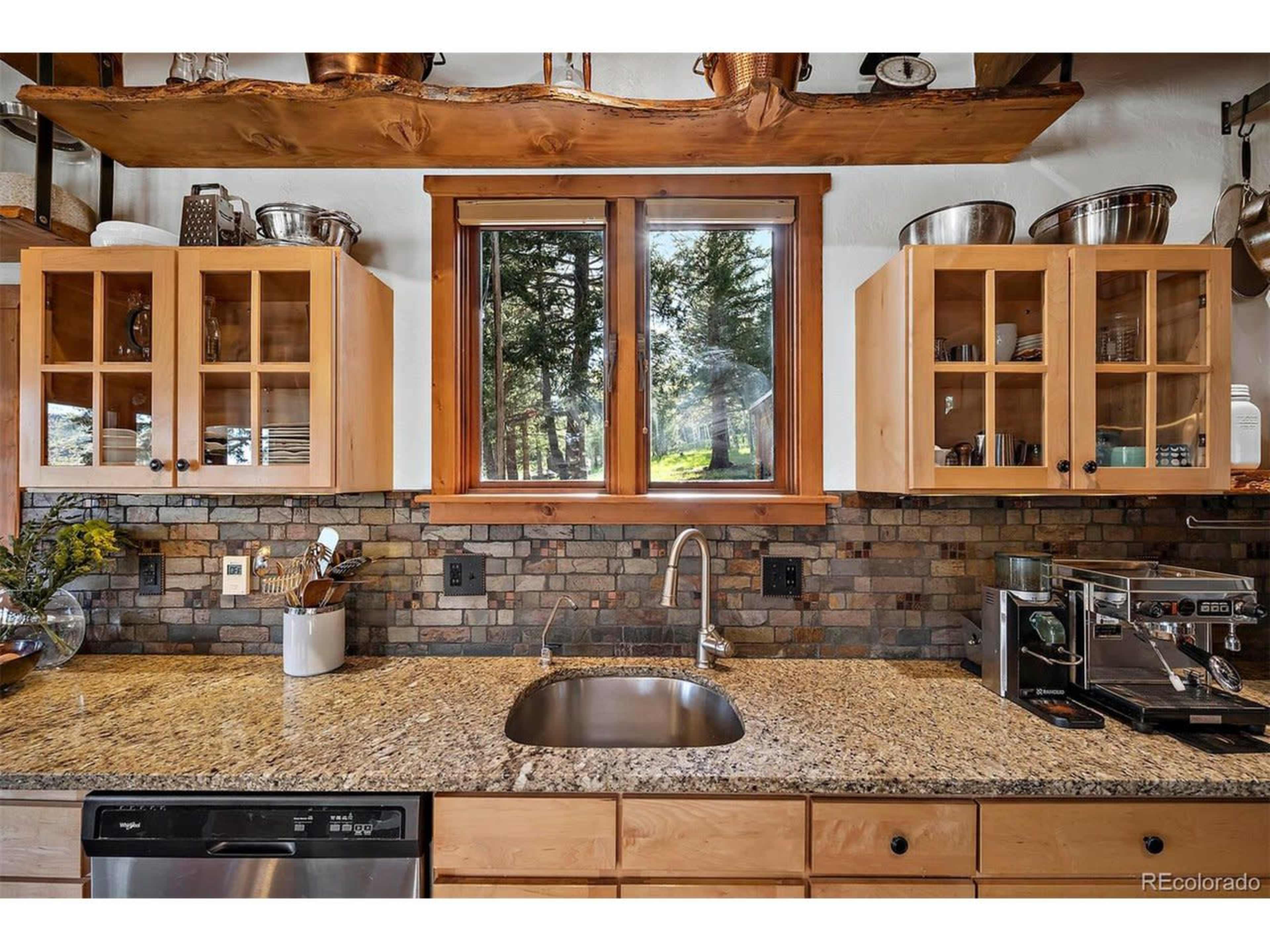 A kitchen with wooden cabinets, a granite countertop, and a window providing natural light, framed by trees outside.