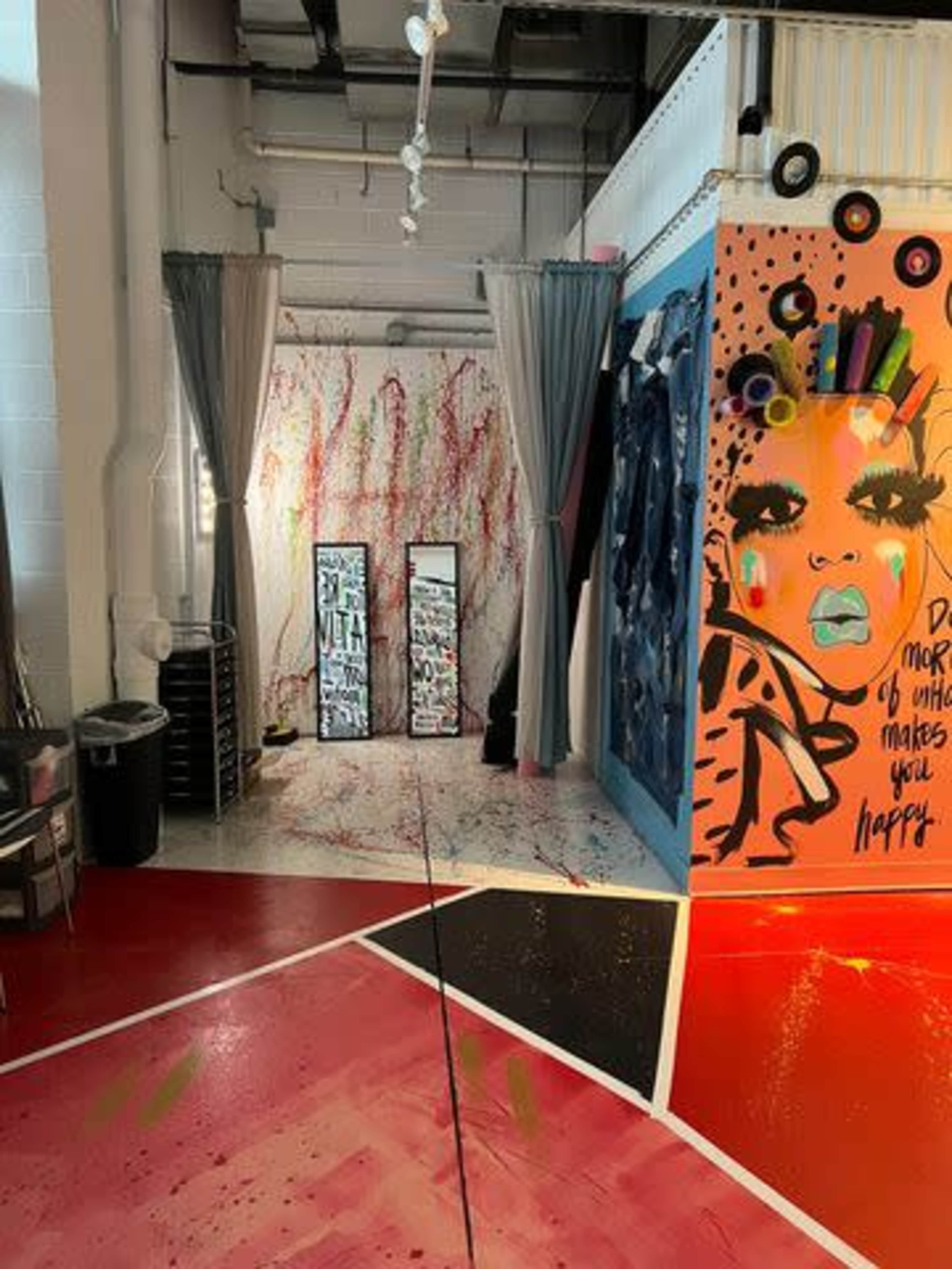 A vibrant, art-filled studio space with bold murals, two mirrored panels, and splashes of paint on the floor.