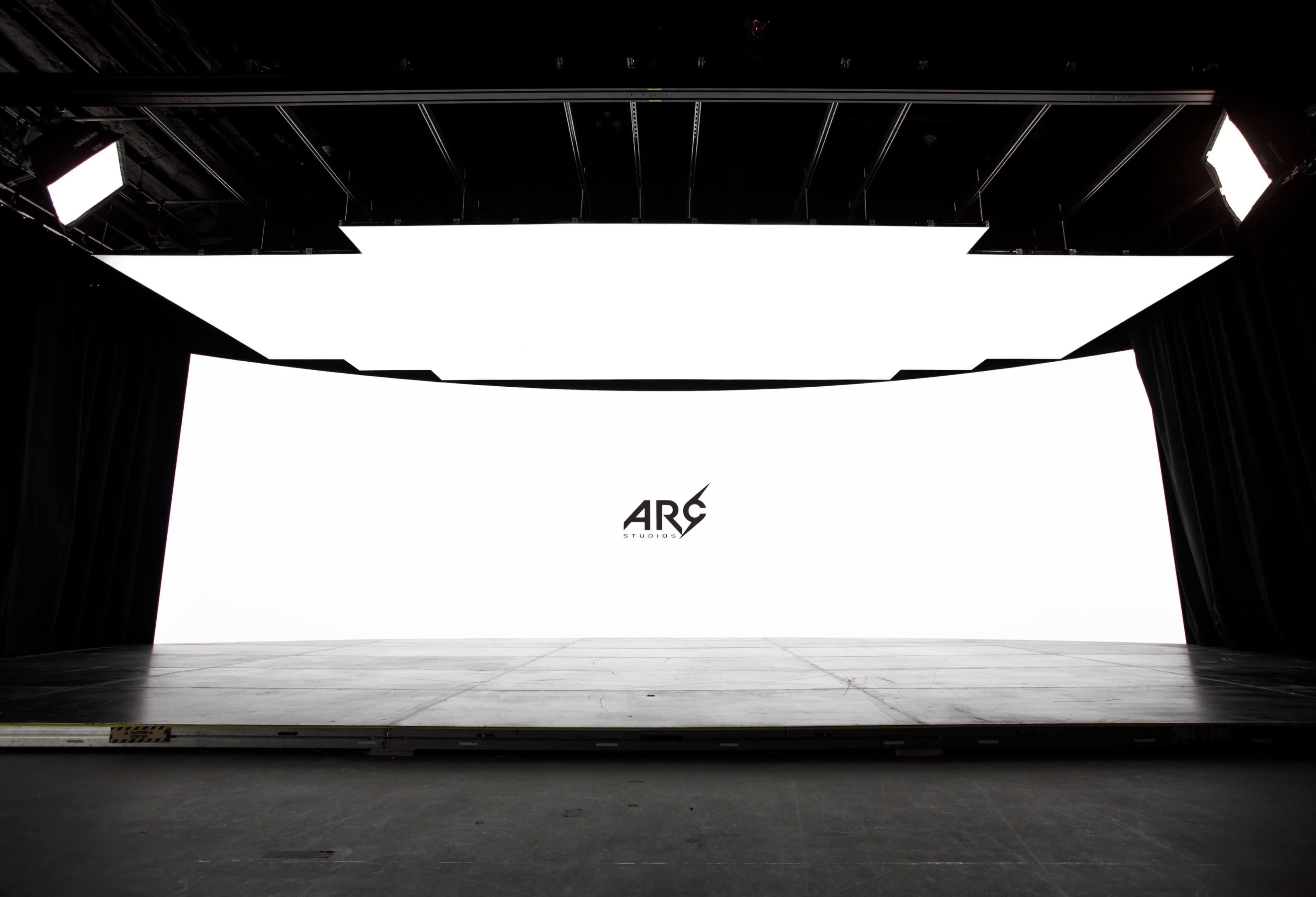 A large, curved white screen with a logo in the center is set against a dark stage with dim lighting.
