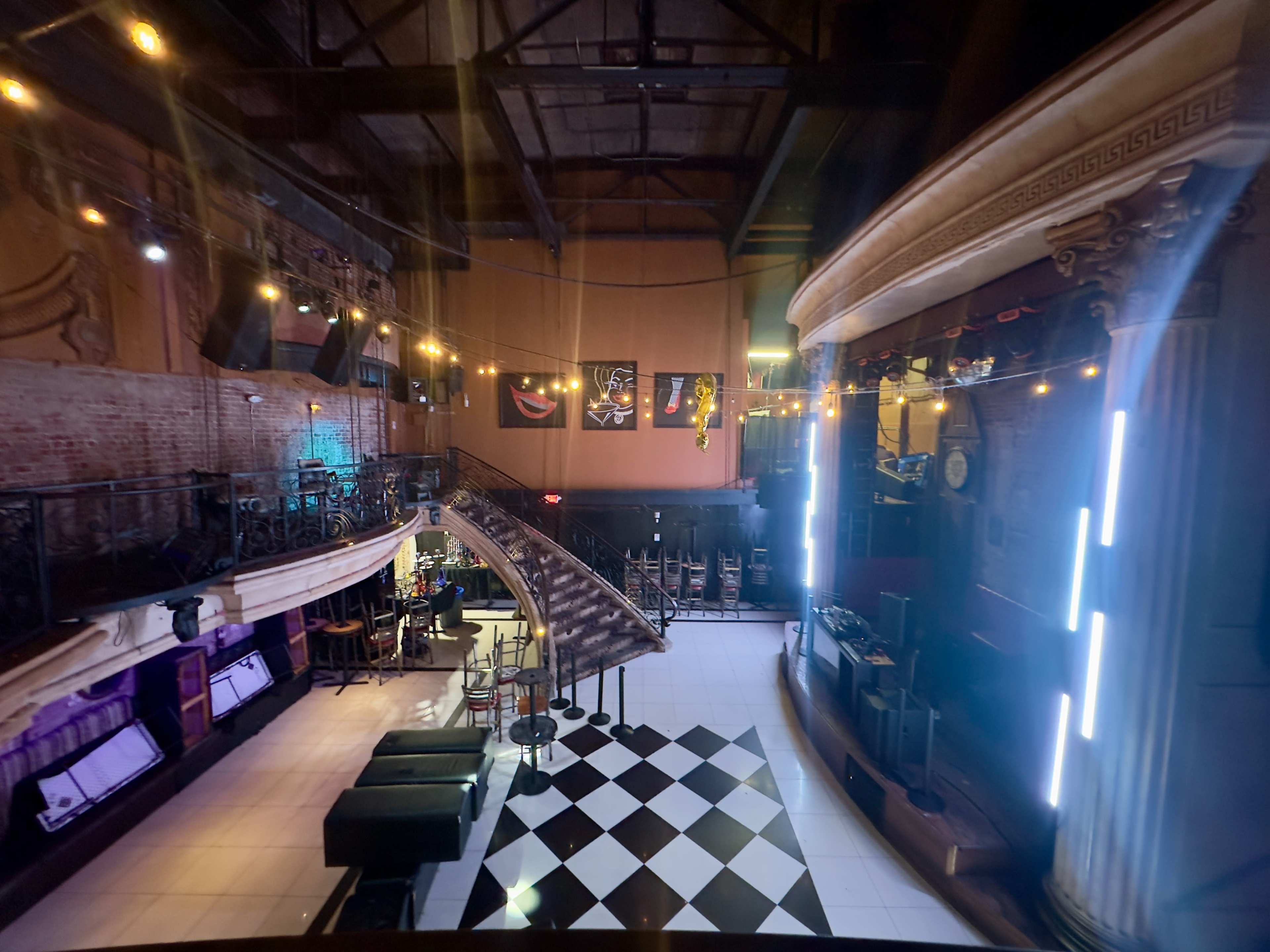 The image shows the interior of a dimly lit venue featuring a staircase, stage area, and checkered floor, with illuminated decorations along the walls.
