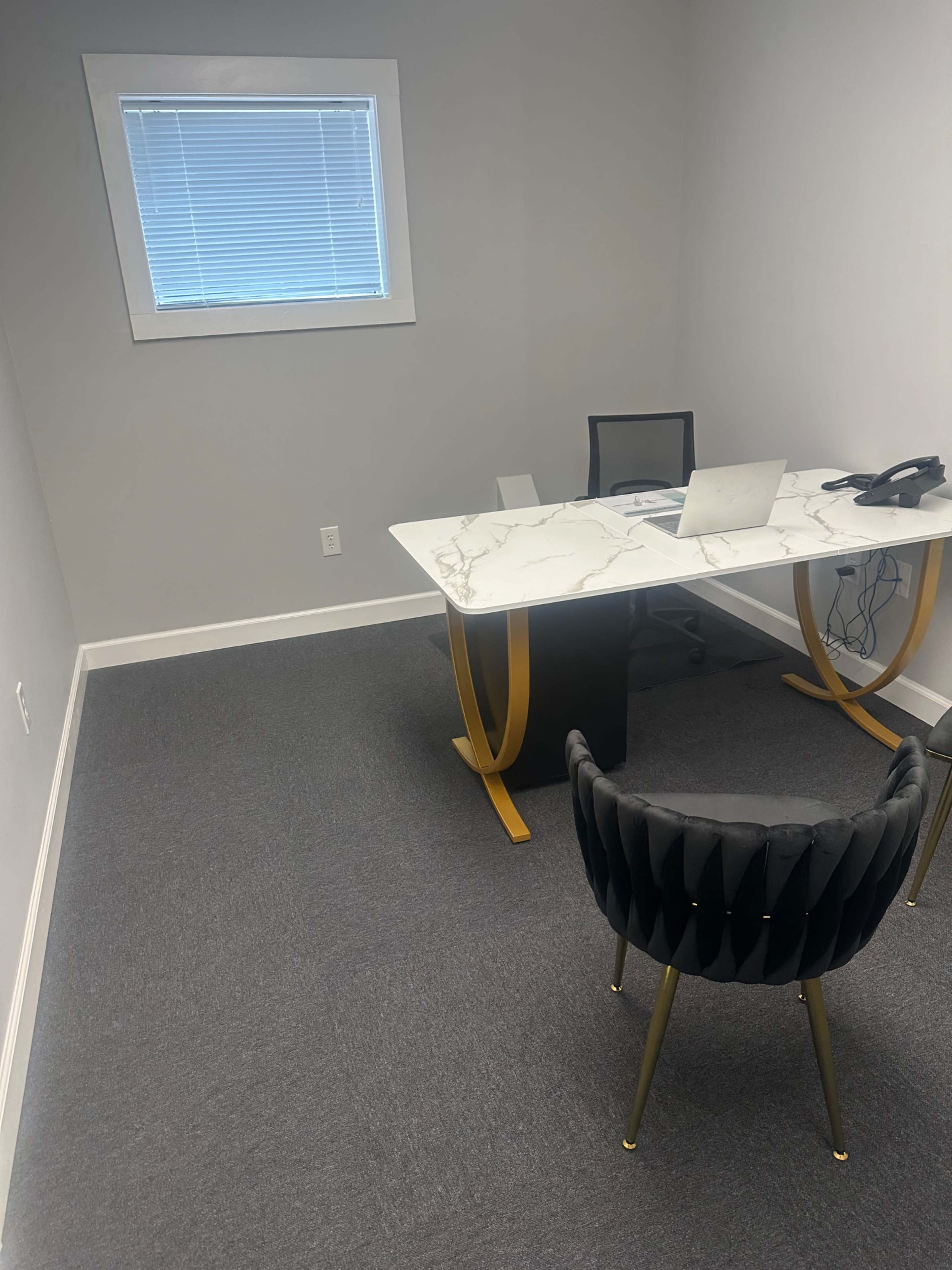 The image shows a minimalistic office with a marble-top desk, a black chair, and a window with blinds.