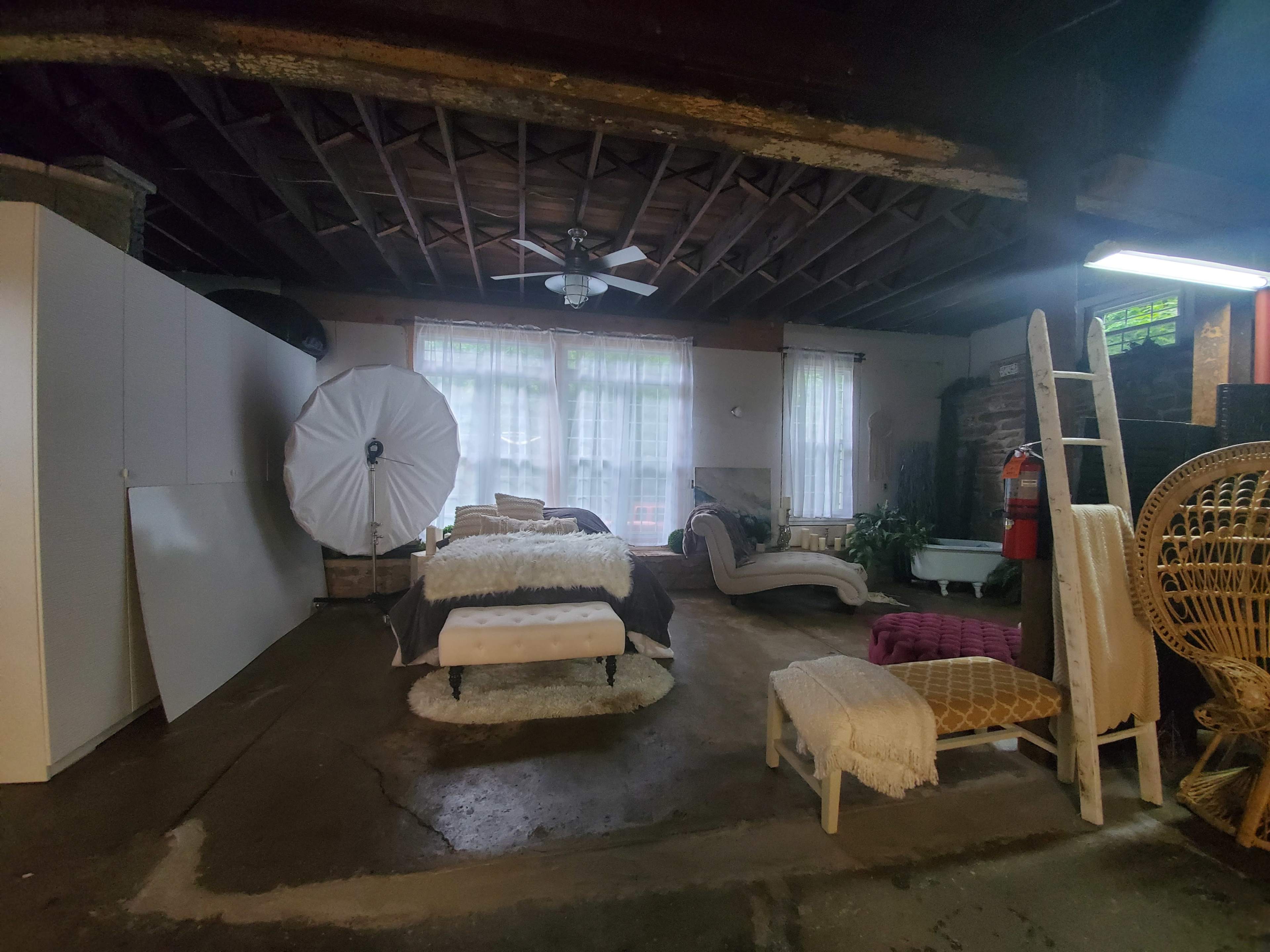 A spacious, unfinished room furnished with various seating arrangements and a large white umbrella leaning against the wall.
