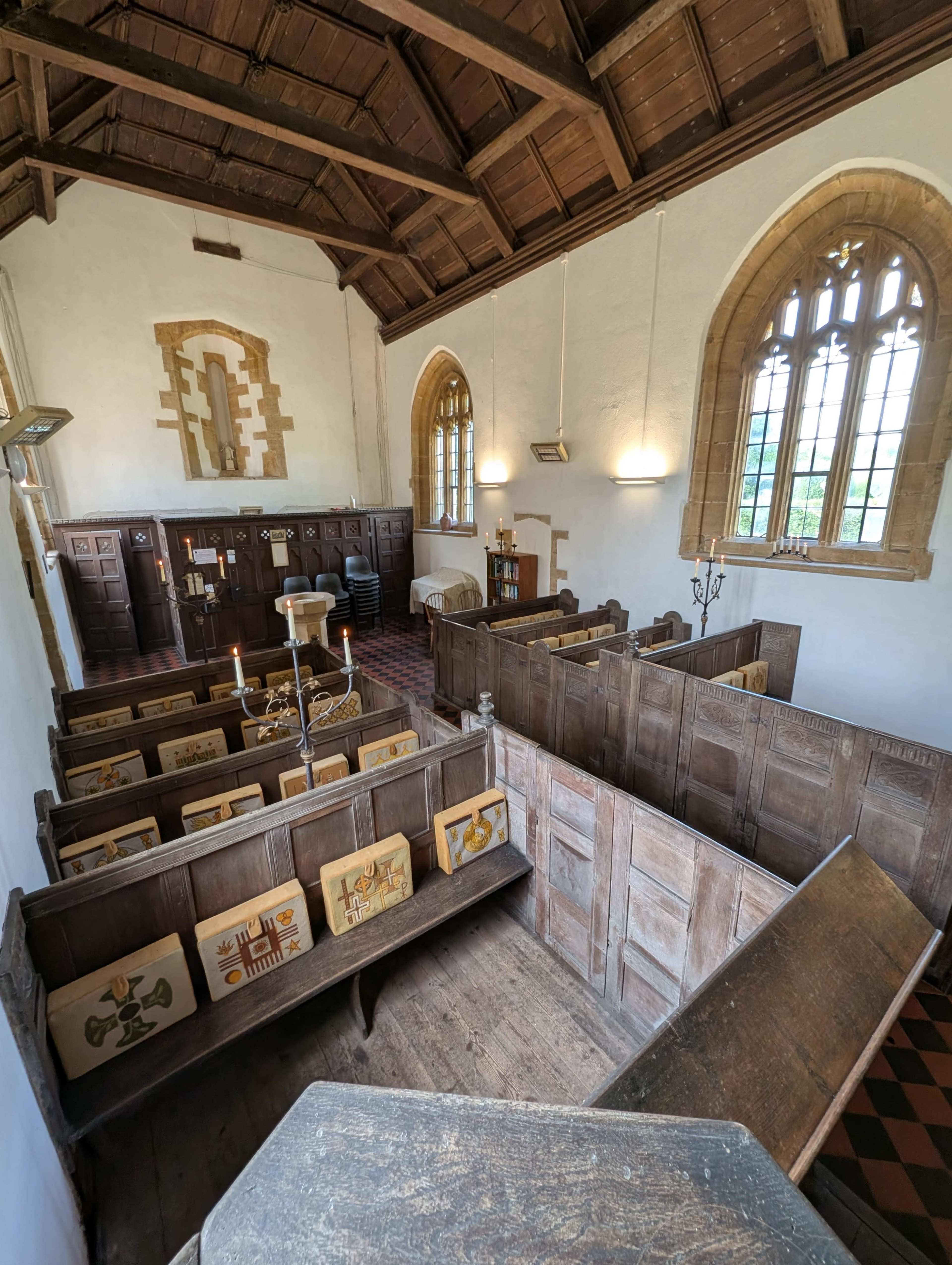 The interior of a historic chapel features wooden pews, stained glass windows, and stone walls, with a view from an elevated angle.