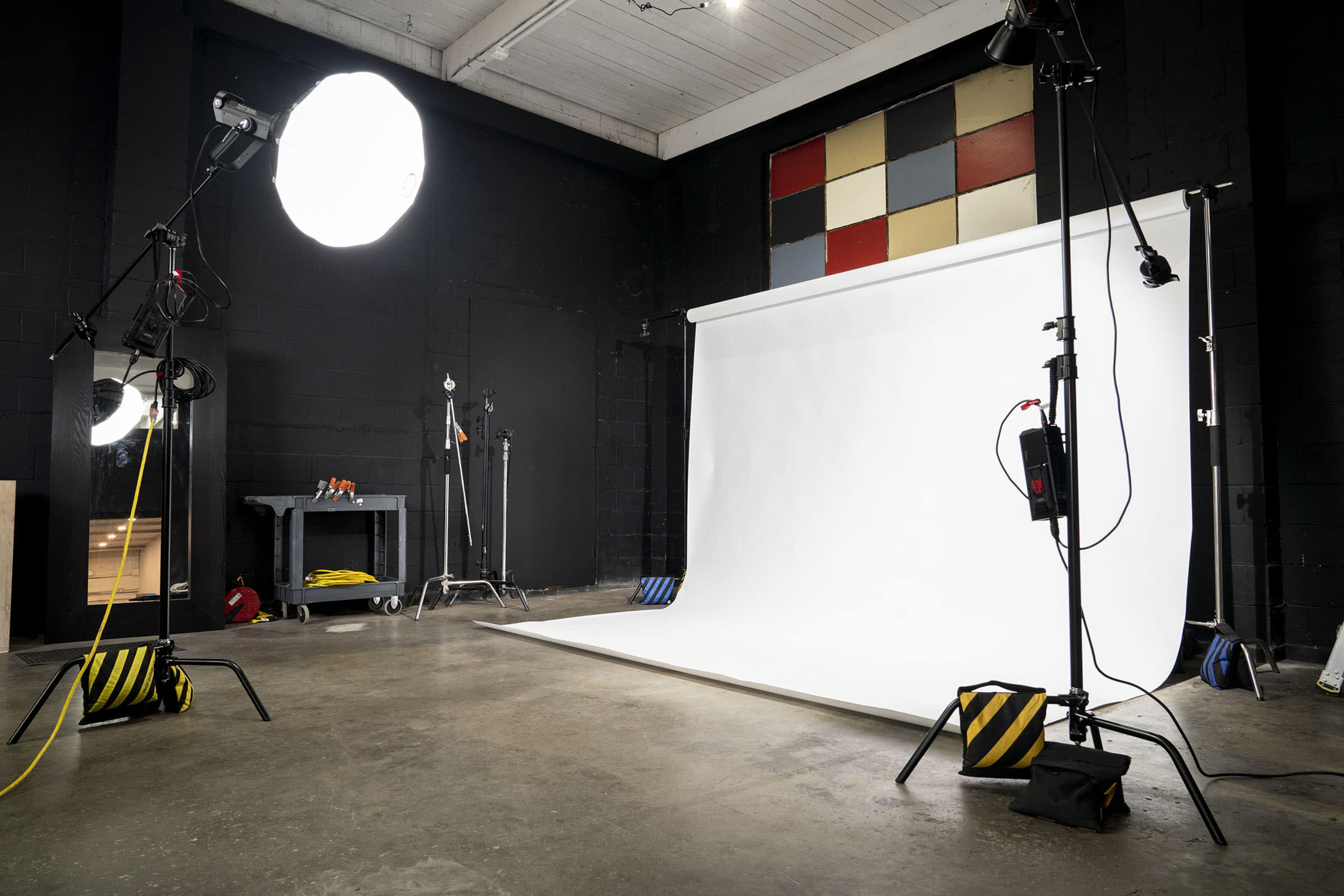 A photography studio with a white backdrop, lighting equipment, and a concrete floor.
