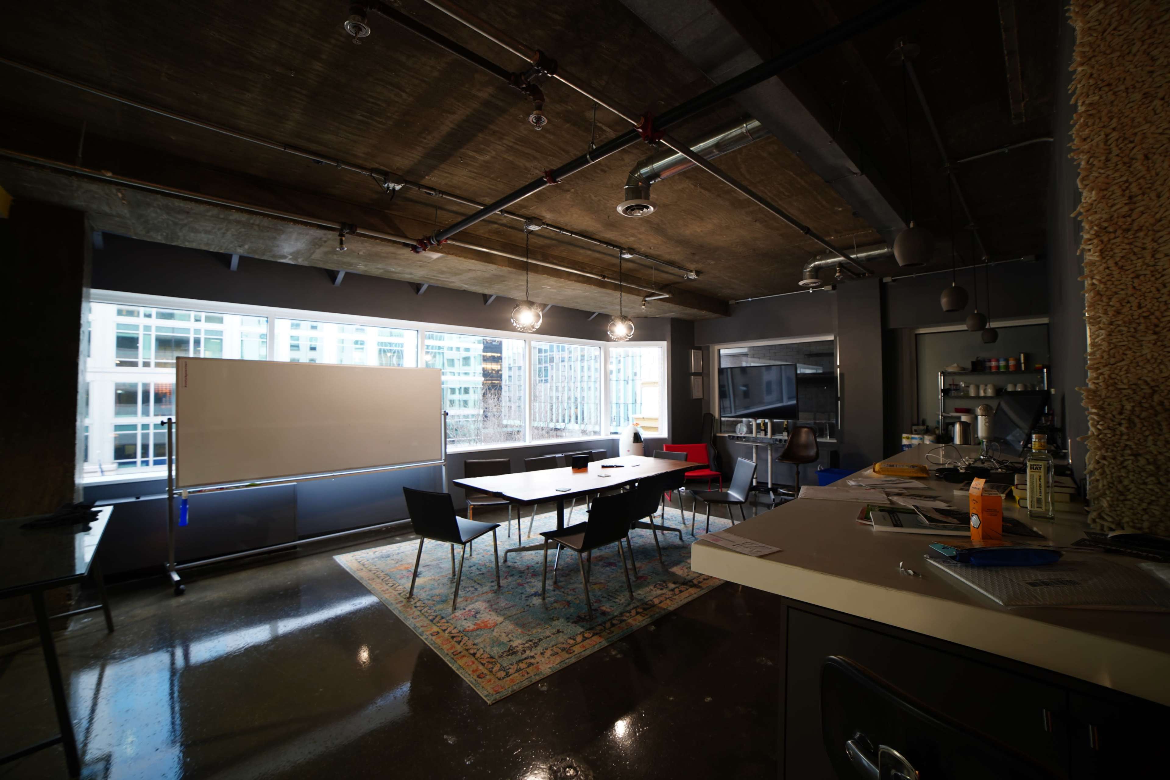 A modern office space featuring a large conference table surrounded by chairs, a whiteboard, and large windows overlooking a cityscape.