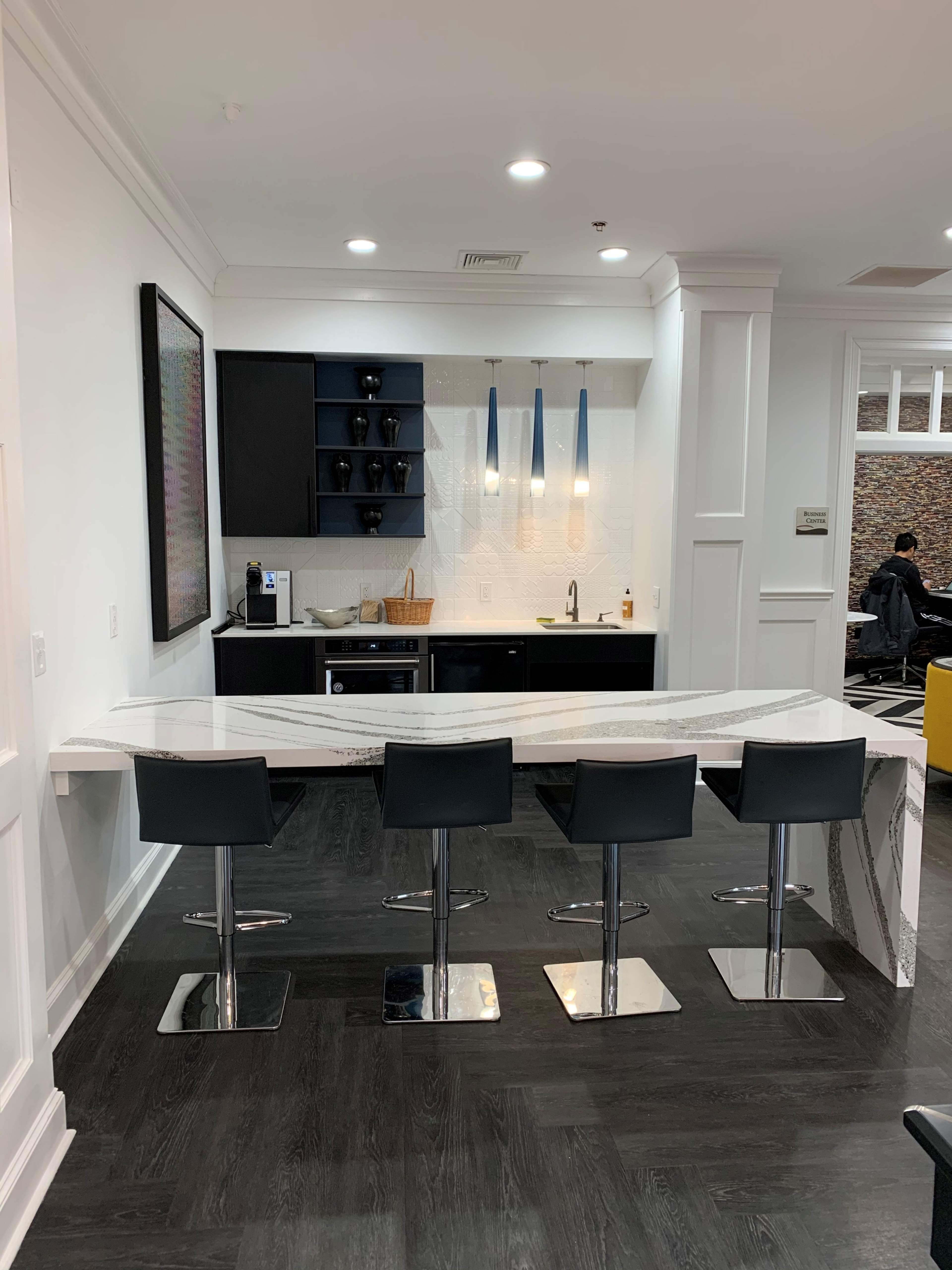 A modern kitchen with a curved countertop and four black bar stools.