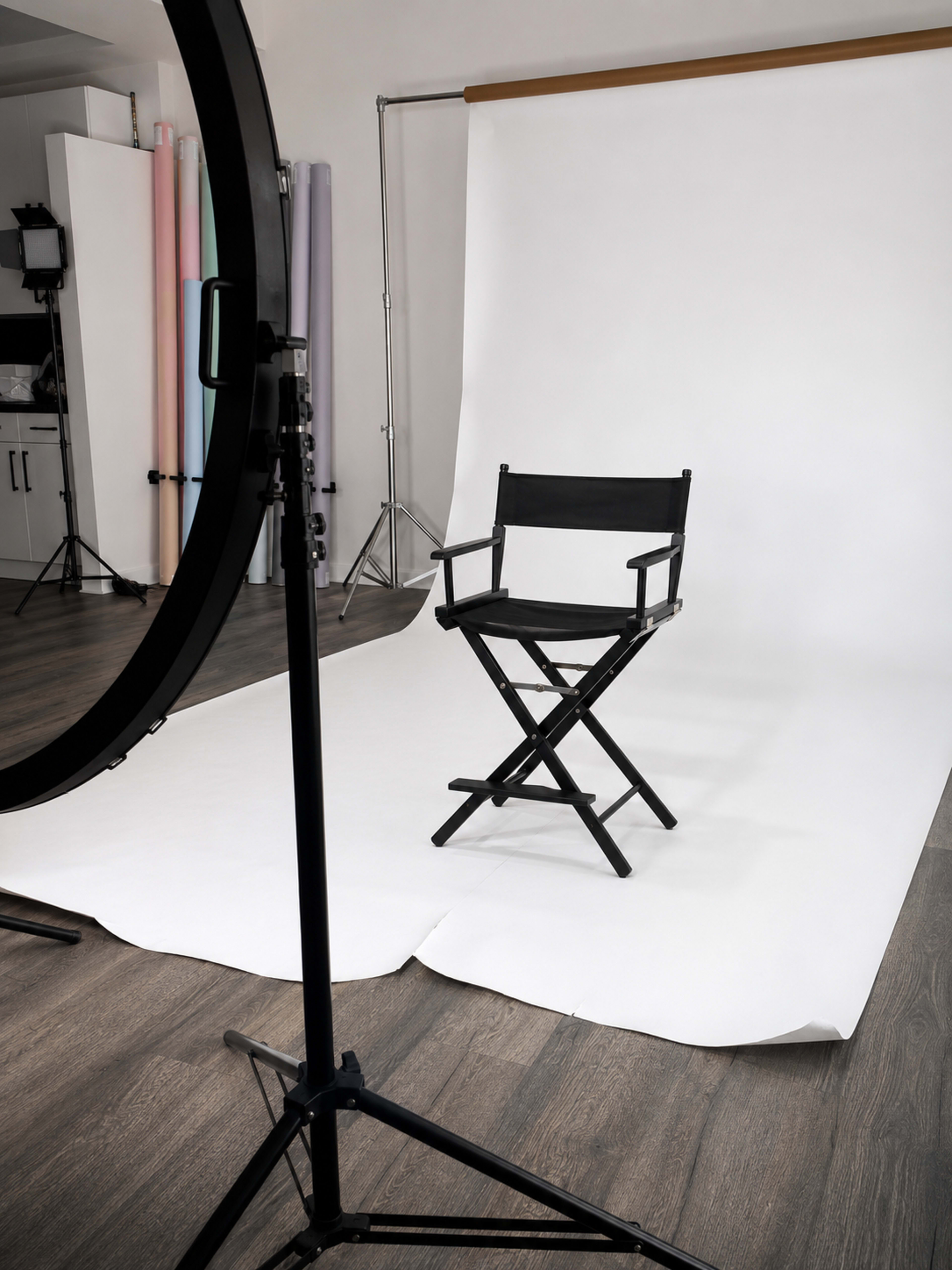 A black director's chair is positioned in front of a white backdrop within a photography studio.