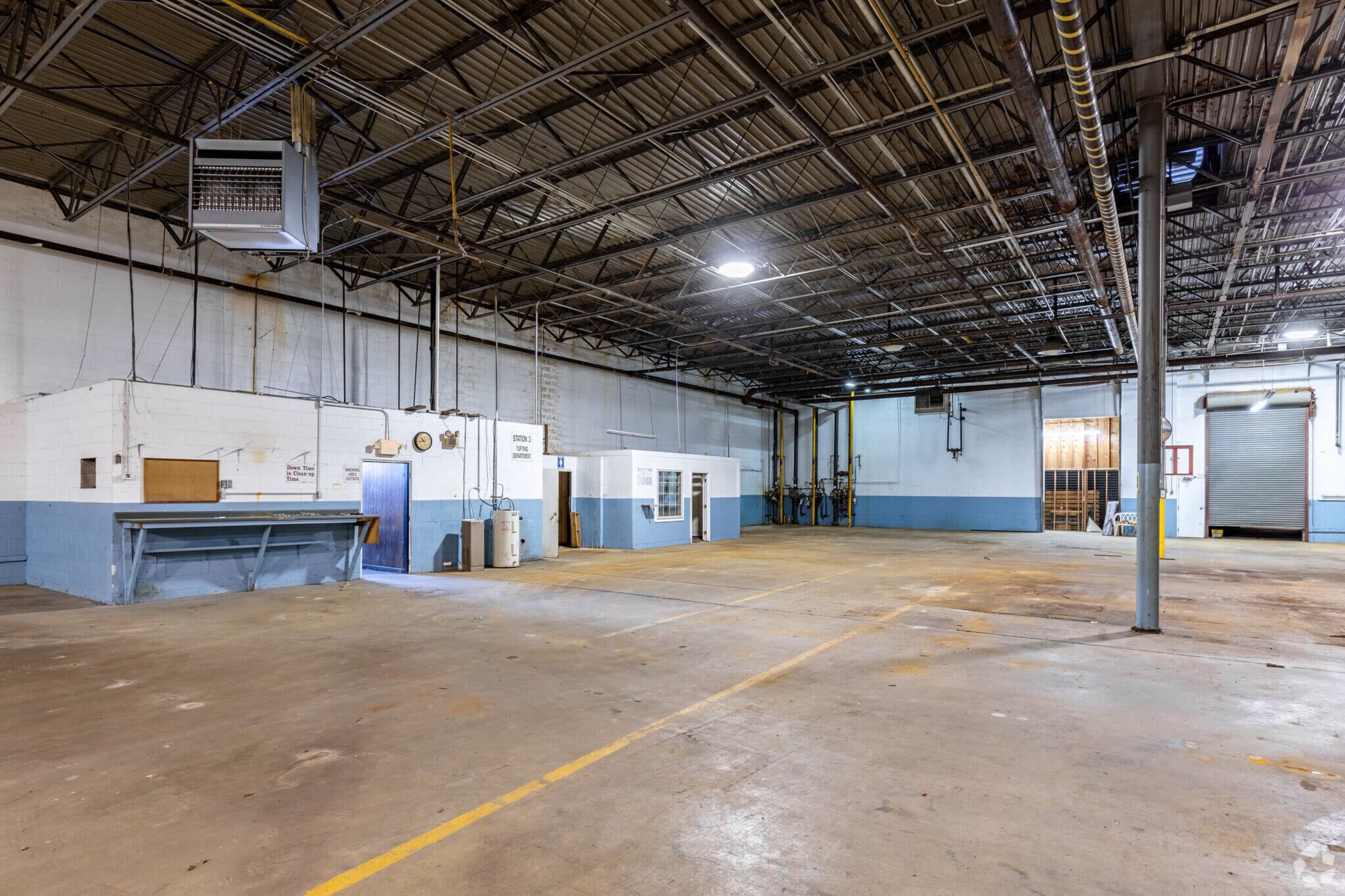 An empty industrial warehouse with a concrete floor and high ceilings, featuring blue-painted walls and overhead lighting.