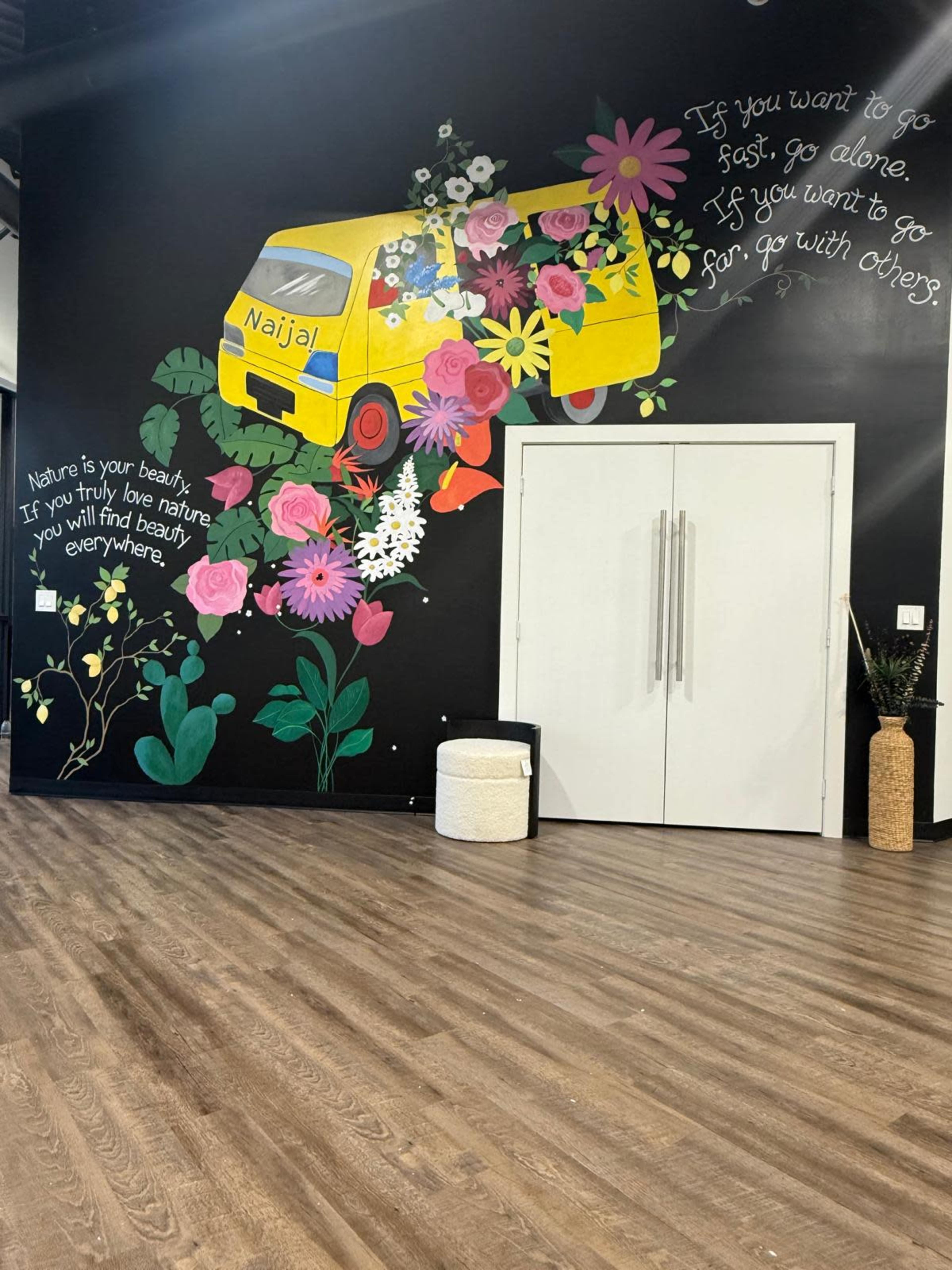 The image shows a mural featuring a yellow van surrounded by colorful flowers on a black wall, alongside a motivational quote.