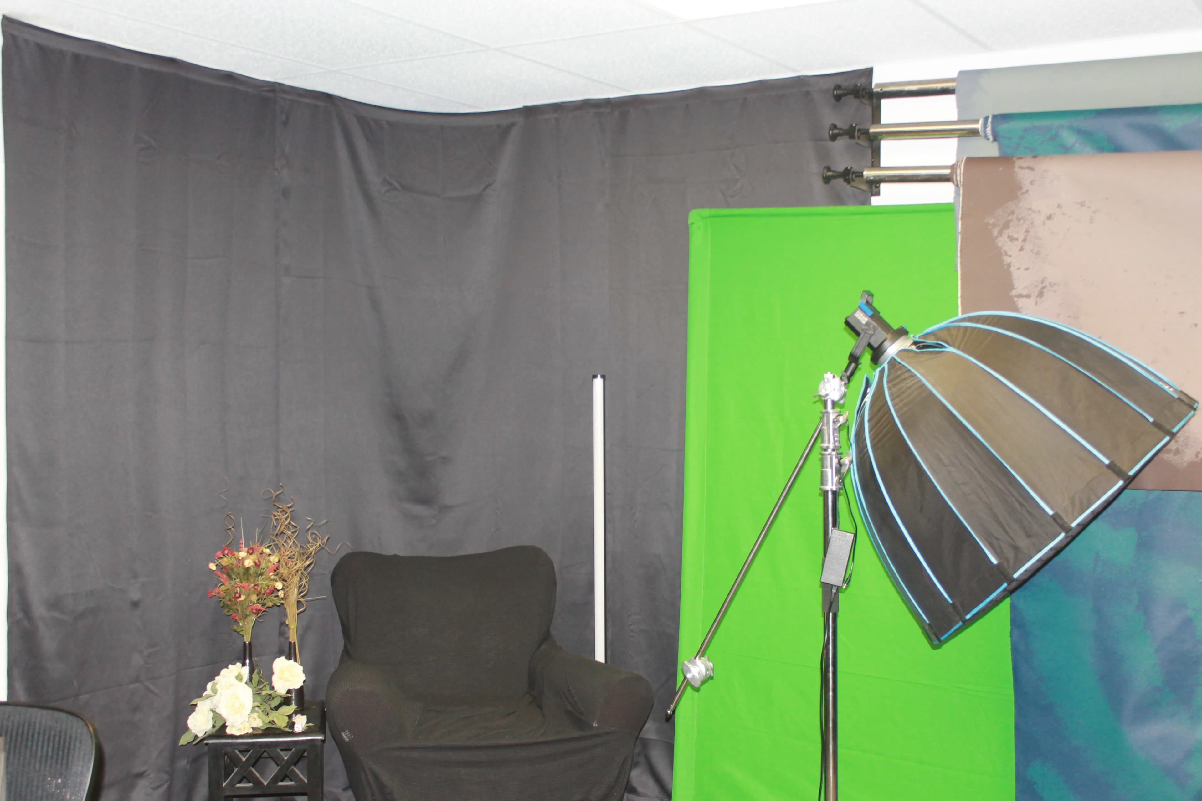 A studio setup with a black curtain, a green backdrop, a chair, and a lighting umbrella on a stand.