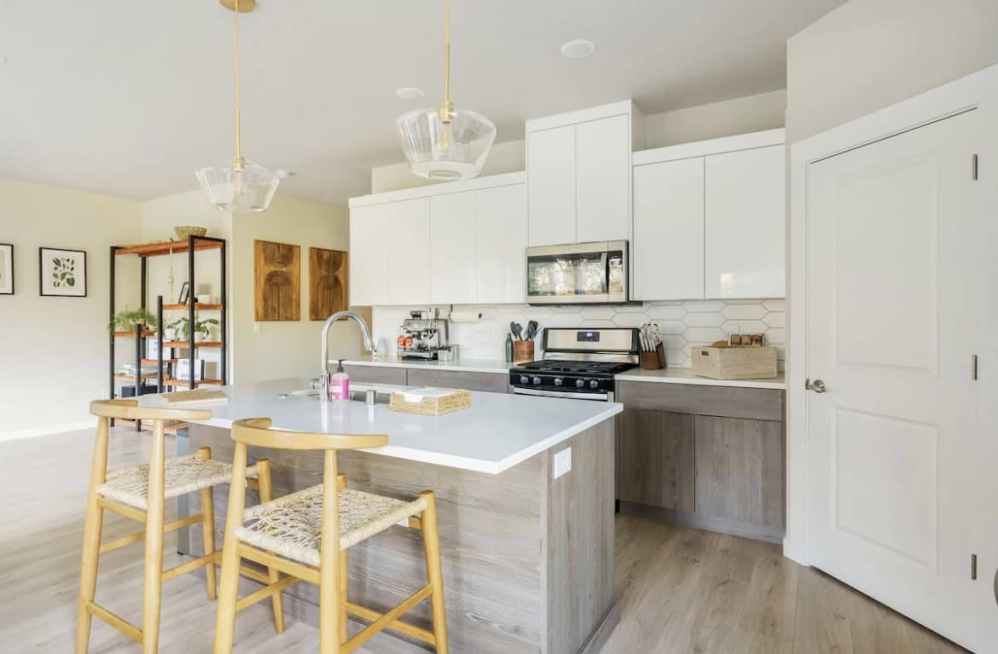 A modern kitchen features white cabinetry, a gray countertop, and wooden barstools, providing a clean and functional space.