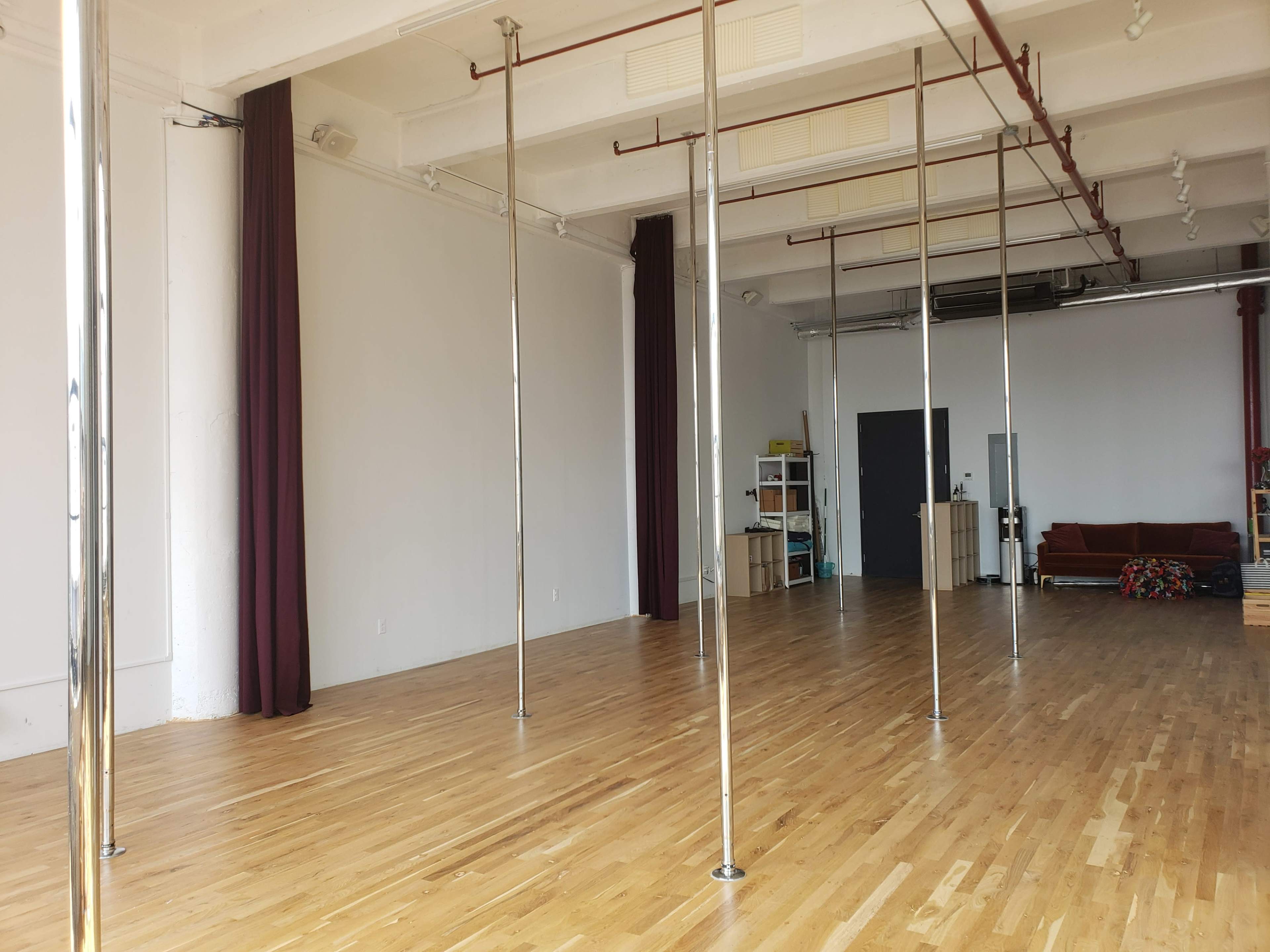 A spacious, empty room with hardwood flooring and several vertical poles placed in a row.