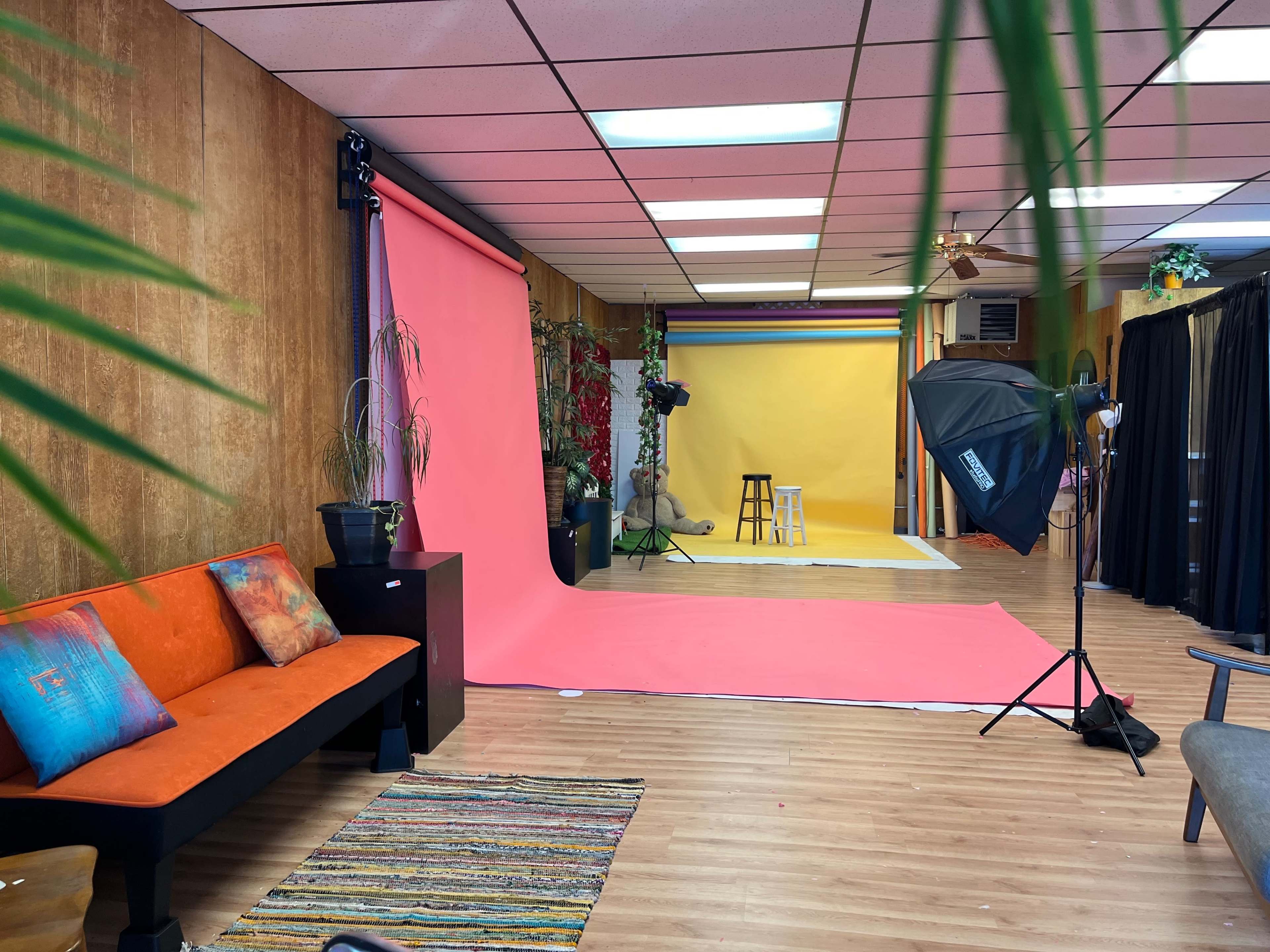 The image shows a spacious studio with colorful backdrops, a couch, and professional lighting equipment set up for photo shoots.