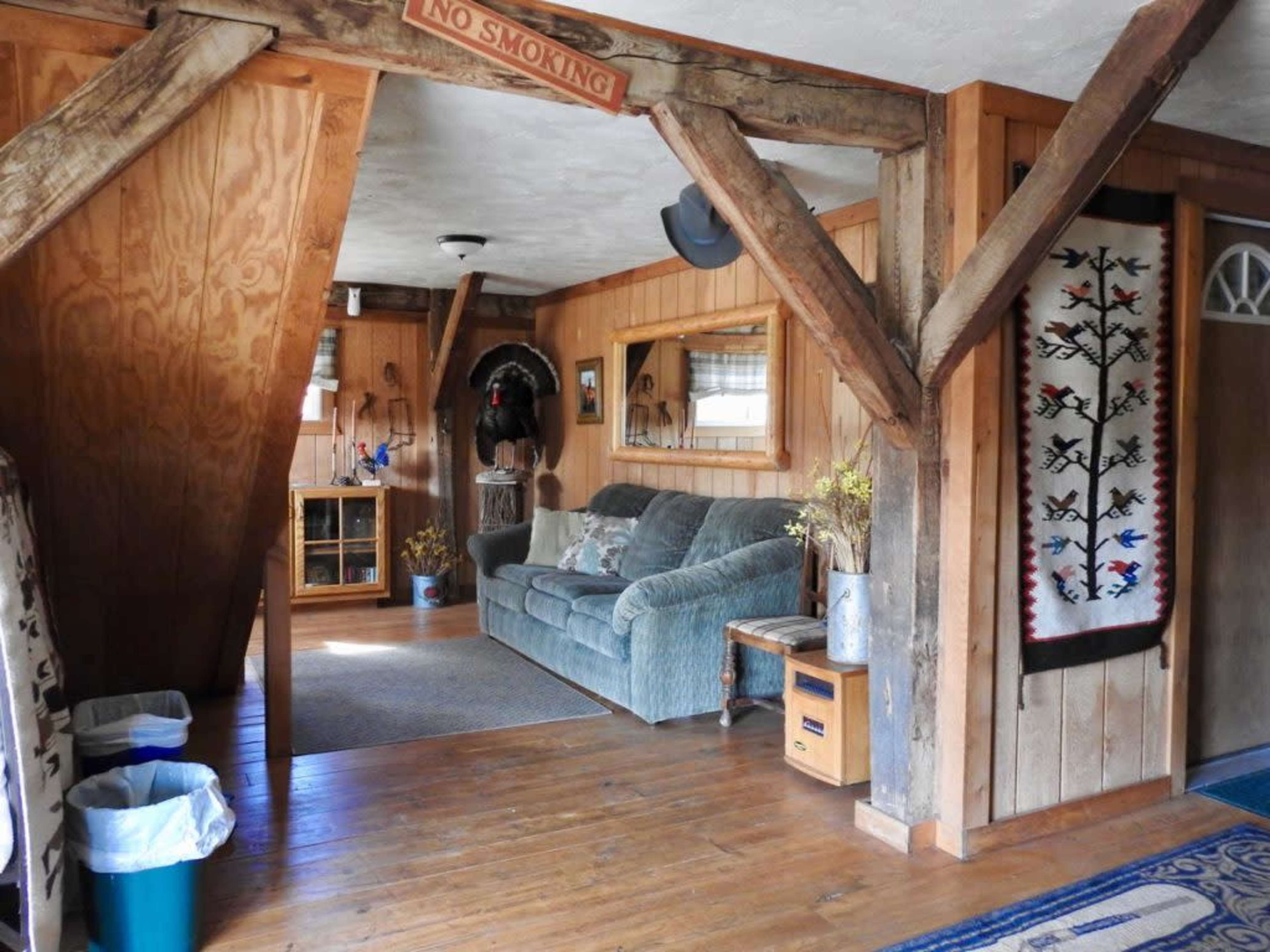 A wooden interior of a room featuring a couch, a wall mirror, a decorative rug, and a framed tapestry.