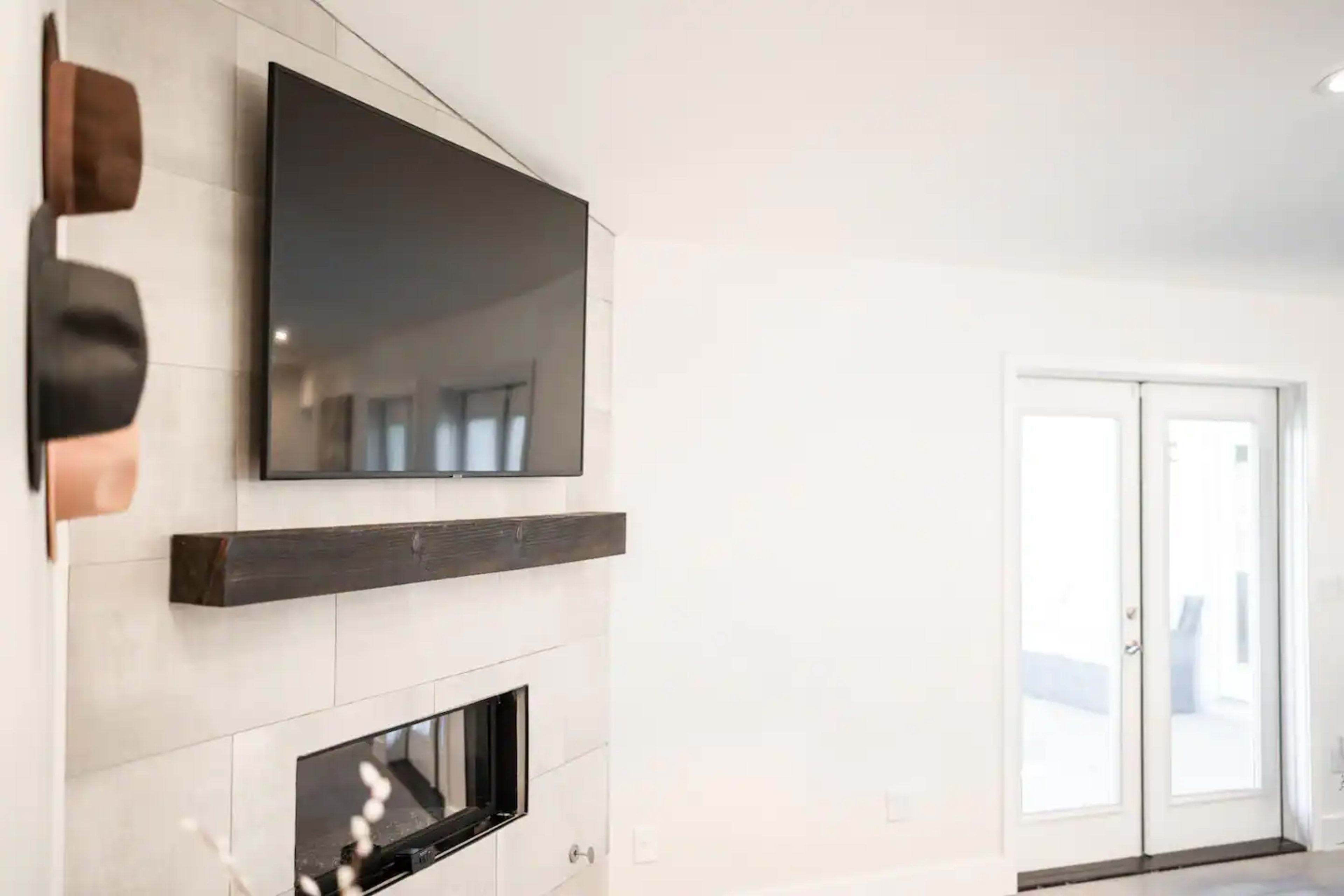 A modern living room with a wall-mounted television above a minimalist fireplace and a set of double glass doors leading outside.