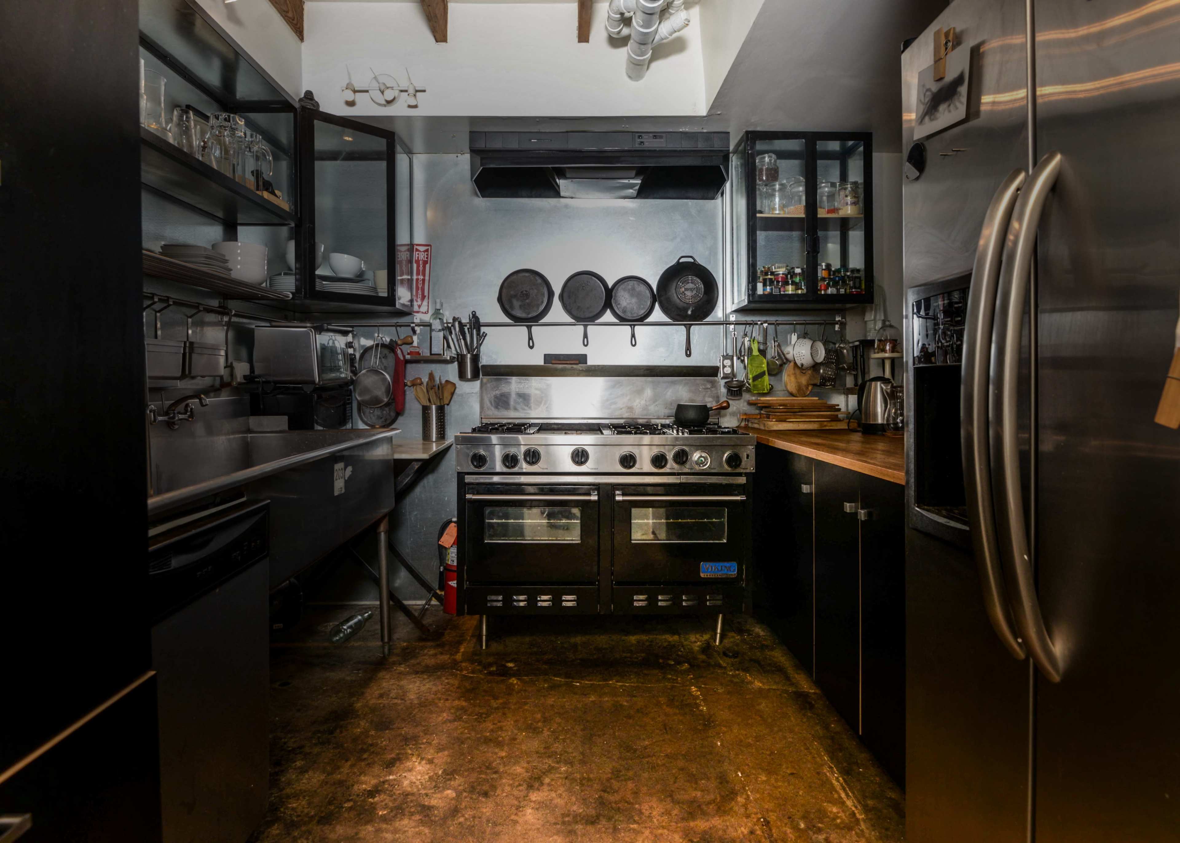 The image shows a modern kitchen with stainless steel appliances, a large stove, and open shelving displaying cooking utensils and spices.