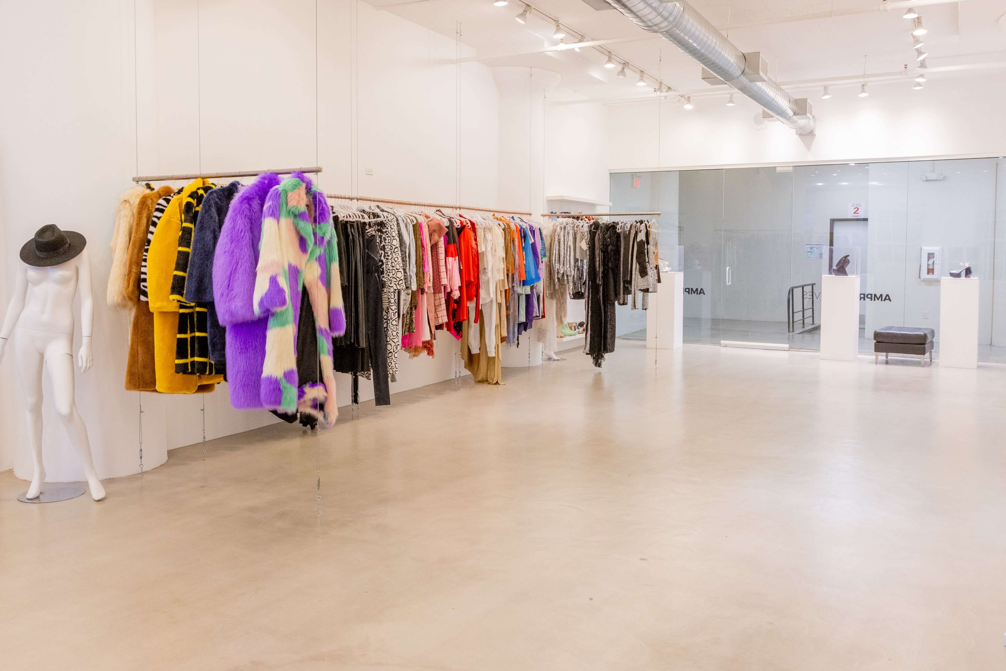 The image shows a modern clothing store interior with a row of colorful fur coats hanging on a rack, alongside a mannequin dressed in a hat.