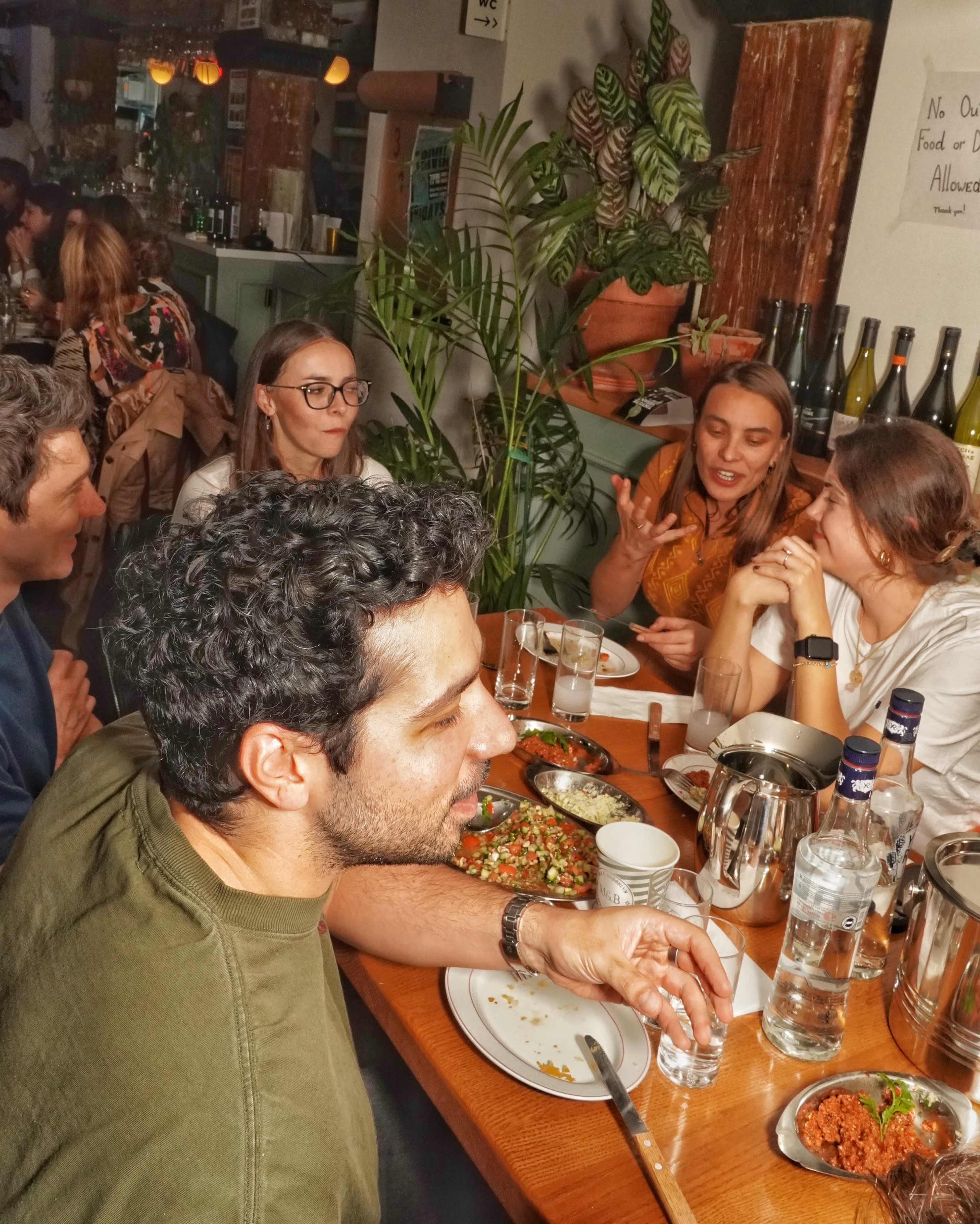 A group of five people sits around a wooden table filled with various dishes in what appears to be a restaurant setting.
