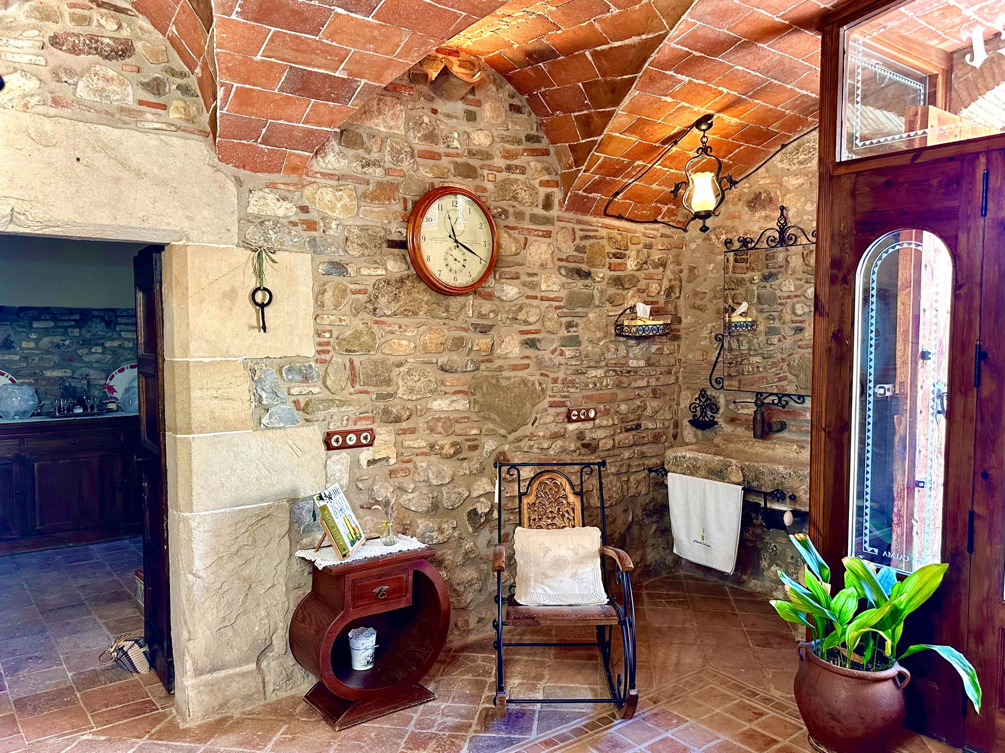 The image depicts a rustic interior with stone walls, a wooden chair, an antique clock, and a small potted plant.