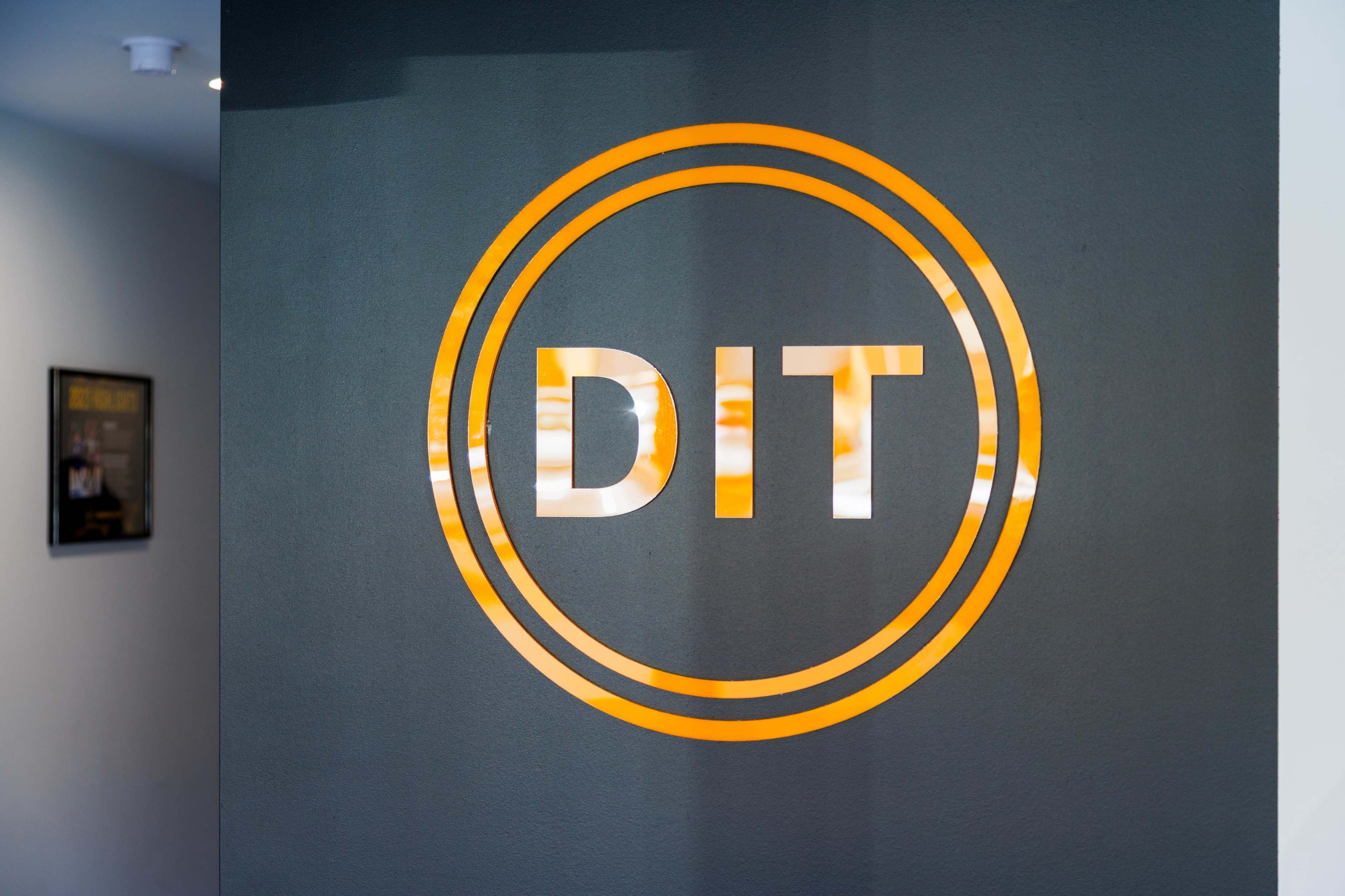 The image shows a circular logo of "DIT" on a dark wall with an orange outline.