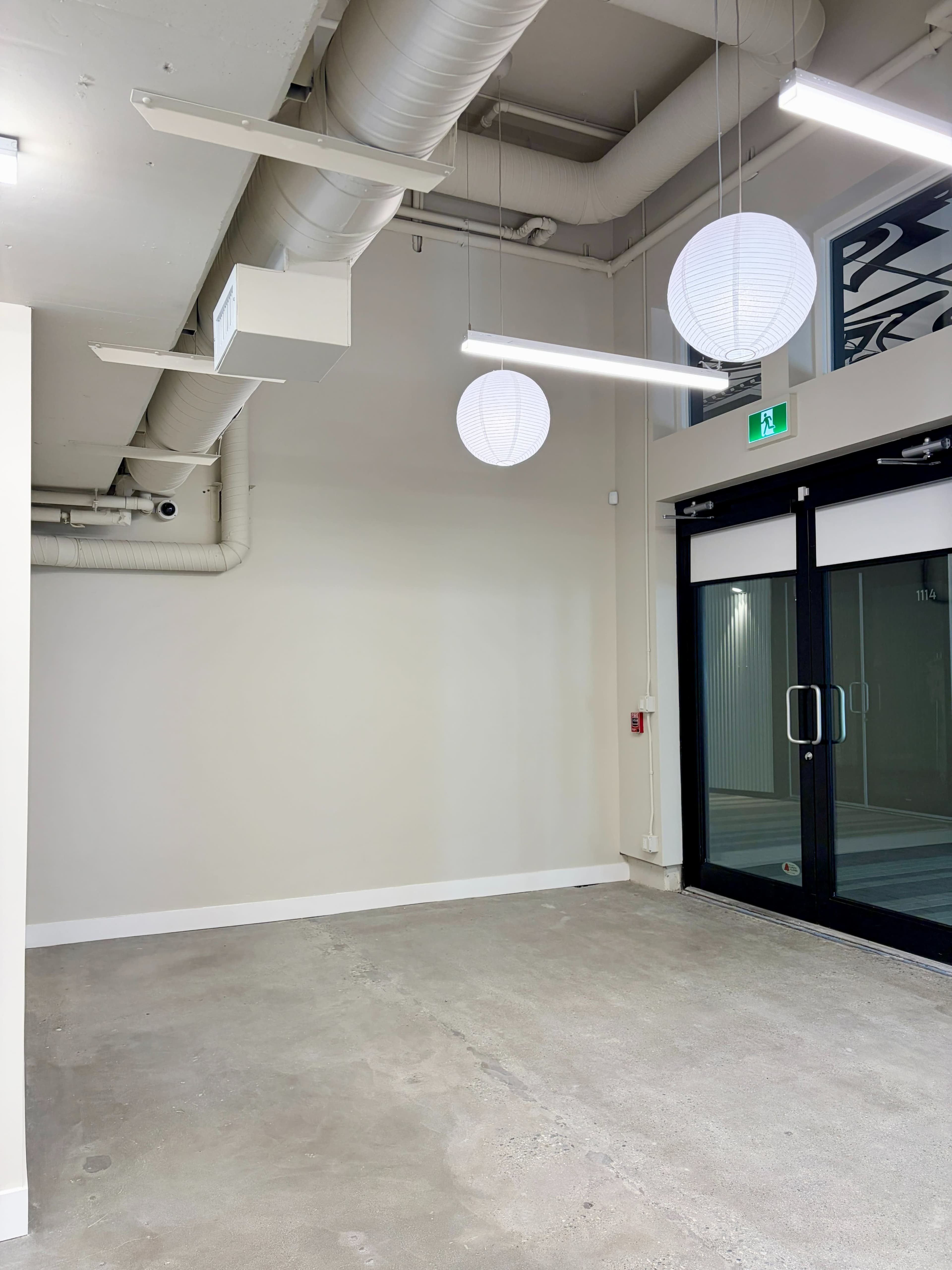The image shows an empty room with concrete flooring, smooth walls, and pendant lights hanging from the ceiling.