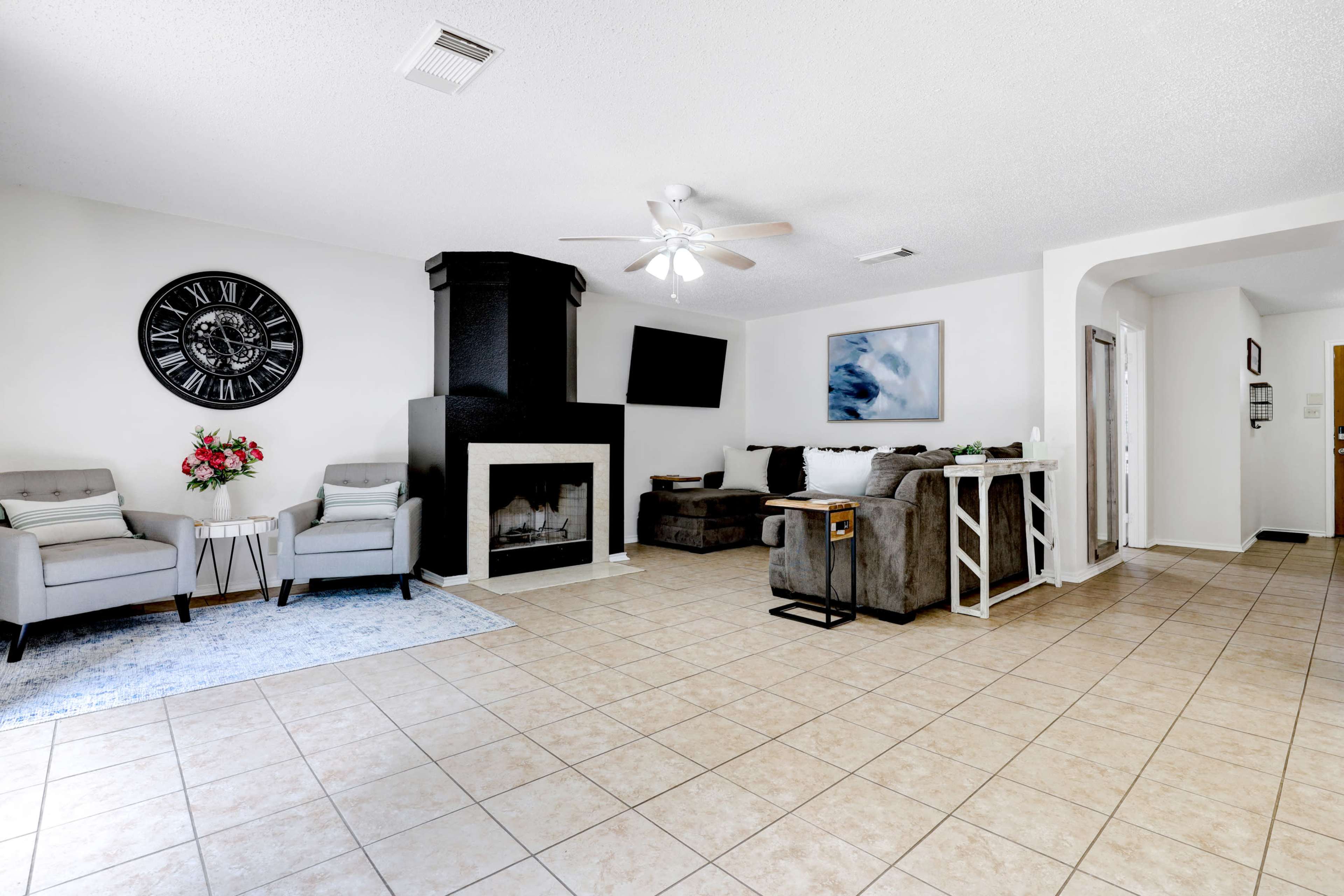 A spacious living room with a black fireplace, a mounted television, two armchairs, and a sectional sofa on tiled flooring.