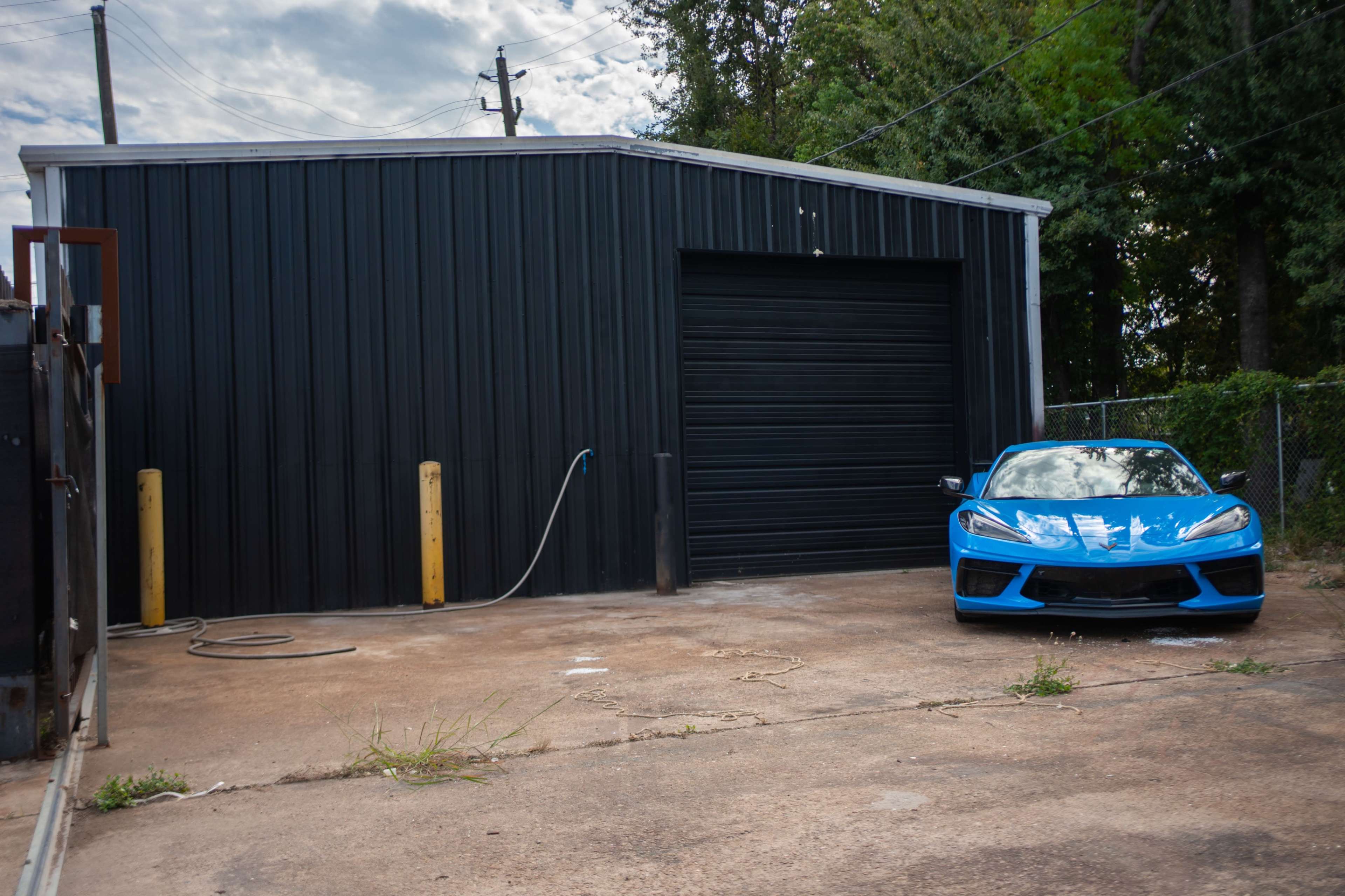 A blue sports car is parked next to a black metal storage building with a closed garage door.