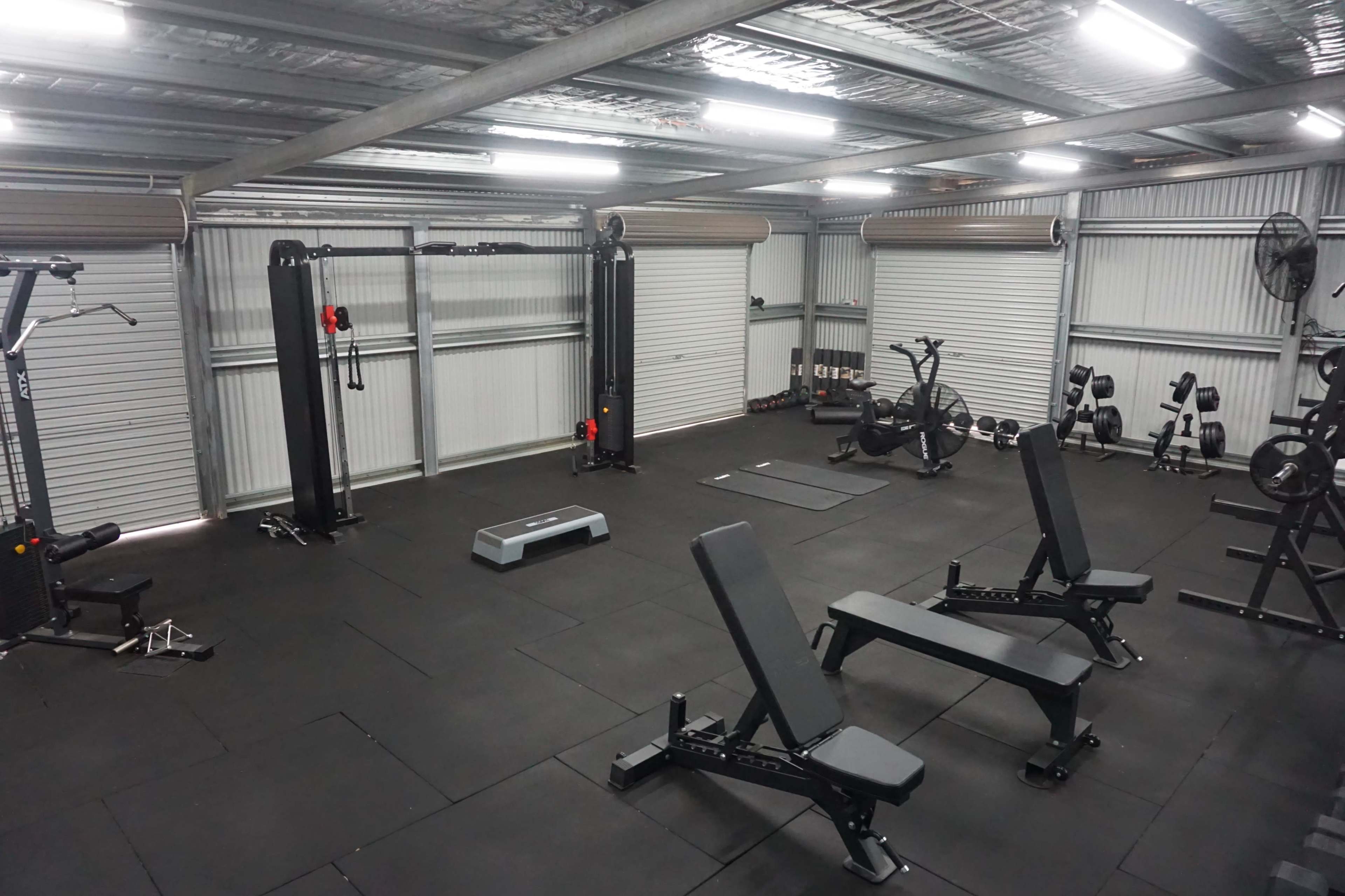 A spacious gym interior equipped with various fitness machines and free weights on a black rubber floor.