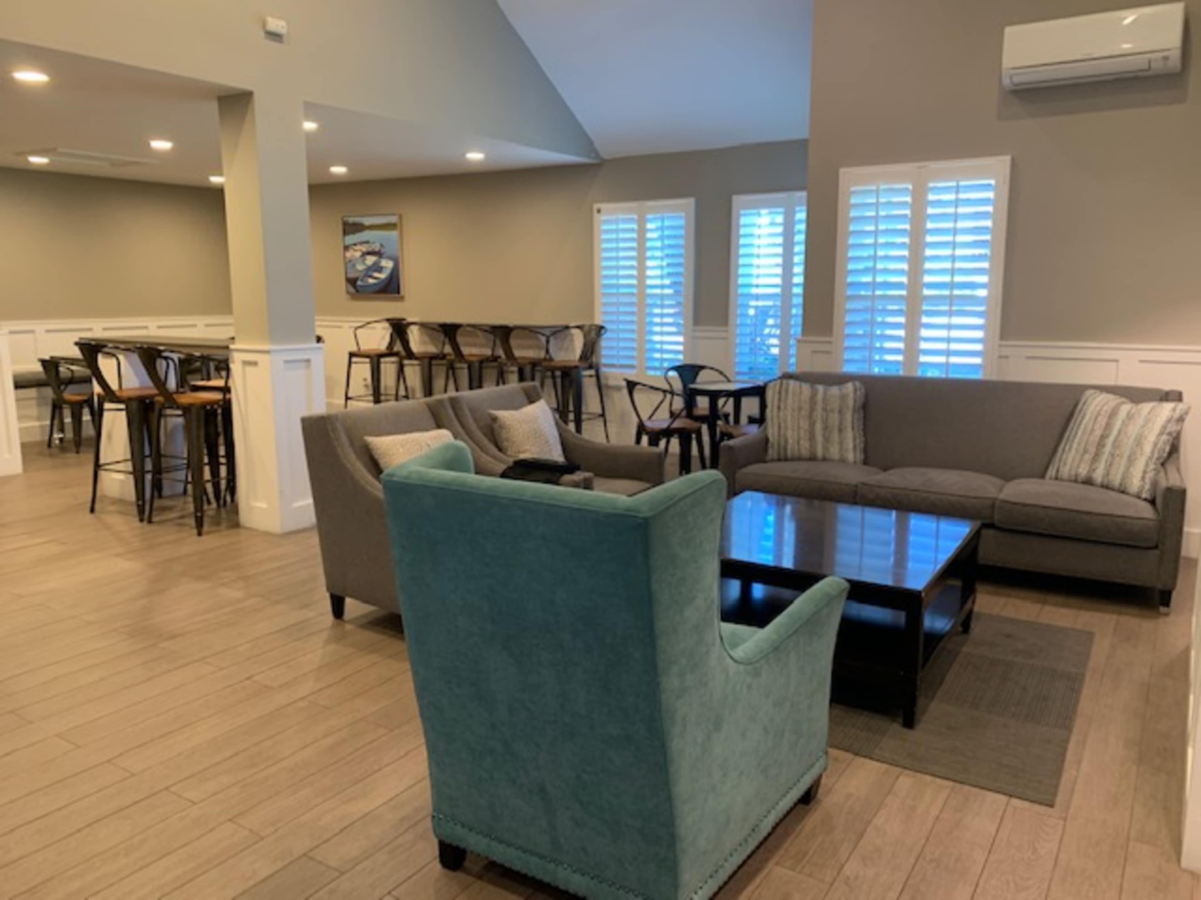 A modern lounge area featuring a grey sectional sofa, a teal armchair, a coffee table, and high tables in the background.